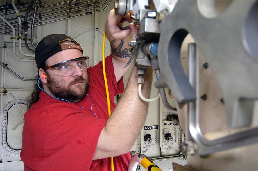 Air Force mechanic Gene Herrington installs a lock crank in the main landing gear area of a Navy E-6 in a Navy hangar at Tinker.  Air Force mechanics routinely lend their years of experience to aid the Navy in maintenance on the aircraft. (Air Force photo/Margo Wright)