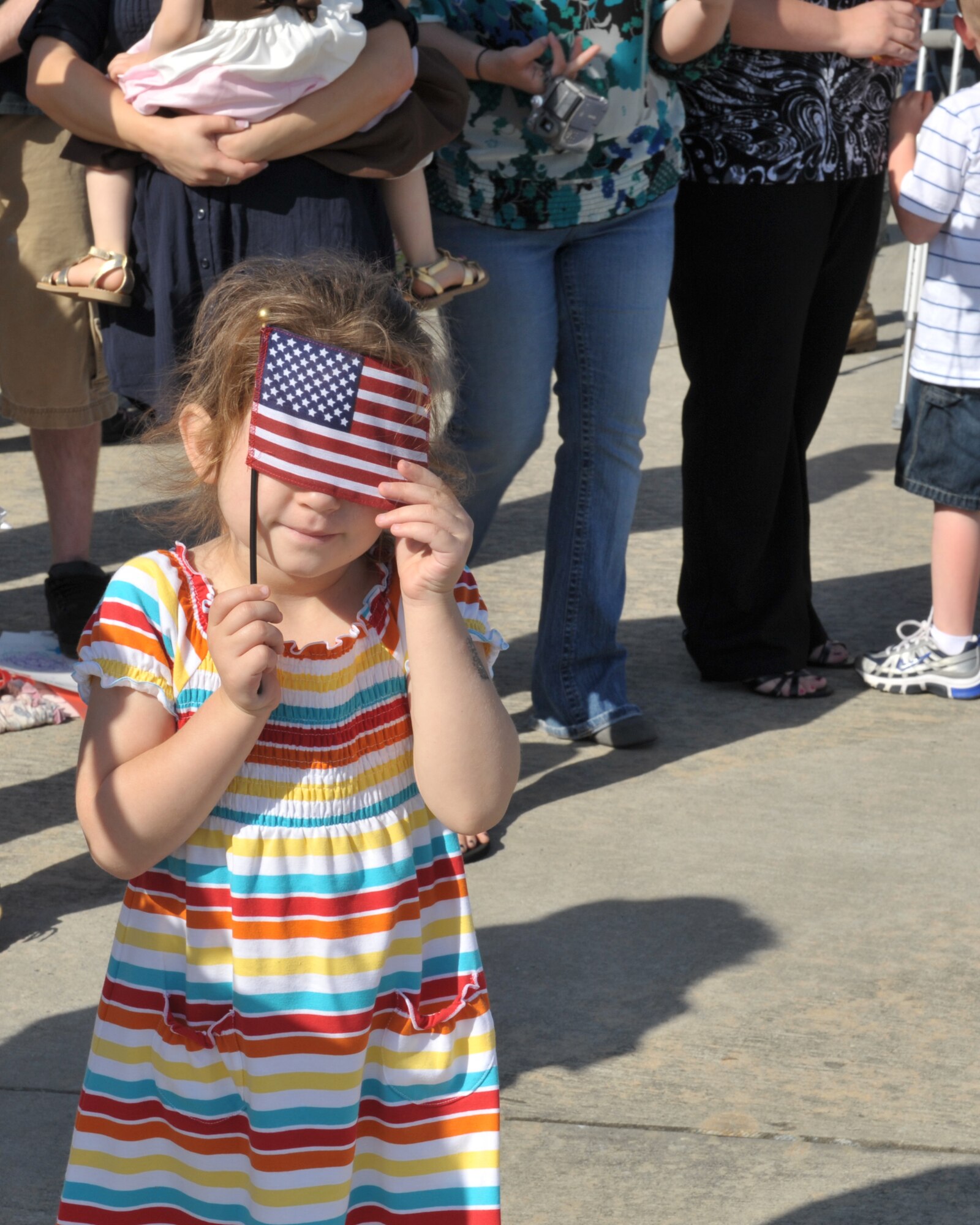 MOODY AIR FORCE BASE, Ga. -- An anxious crowd gathers outside of a C-130 hangar to watch the arrival of about 300 Airmen returning from deployment here March 9. Waiting for a first glimpse of the aircraft, a child uses the American flag to help cover her eyes from the bright sunlight. (U.S. Air Force photo by Senior Airman Javier Cruz Jr.)
