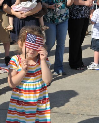 MOODY AIR FORCE BASE, Ga. -- An anxious crowd gathers outside of a C-130 hangar to watch the arrival of about 300 Airmen returning from deployment here March 9. Waiting for a first glimpse of the aircraft, a child uses the American flag to help cover her eyes from the bright sunlight. (U.S. Air Force photo by Senior Airman Javier Cruz Jr.)