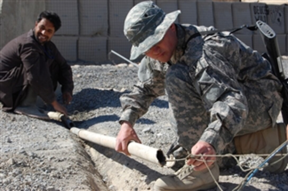 U.S. Army Spc. Christopher Kroneberger (right) helps an Afghan man lay cable at Forward Operating Base Lagman, Afghanistan, on March 4, 2009.  