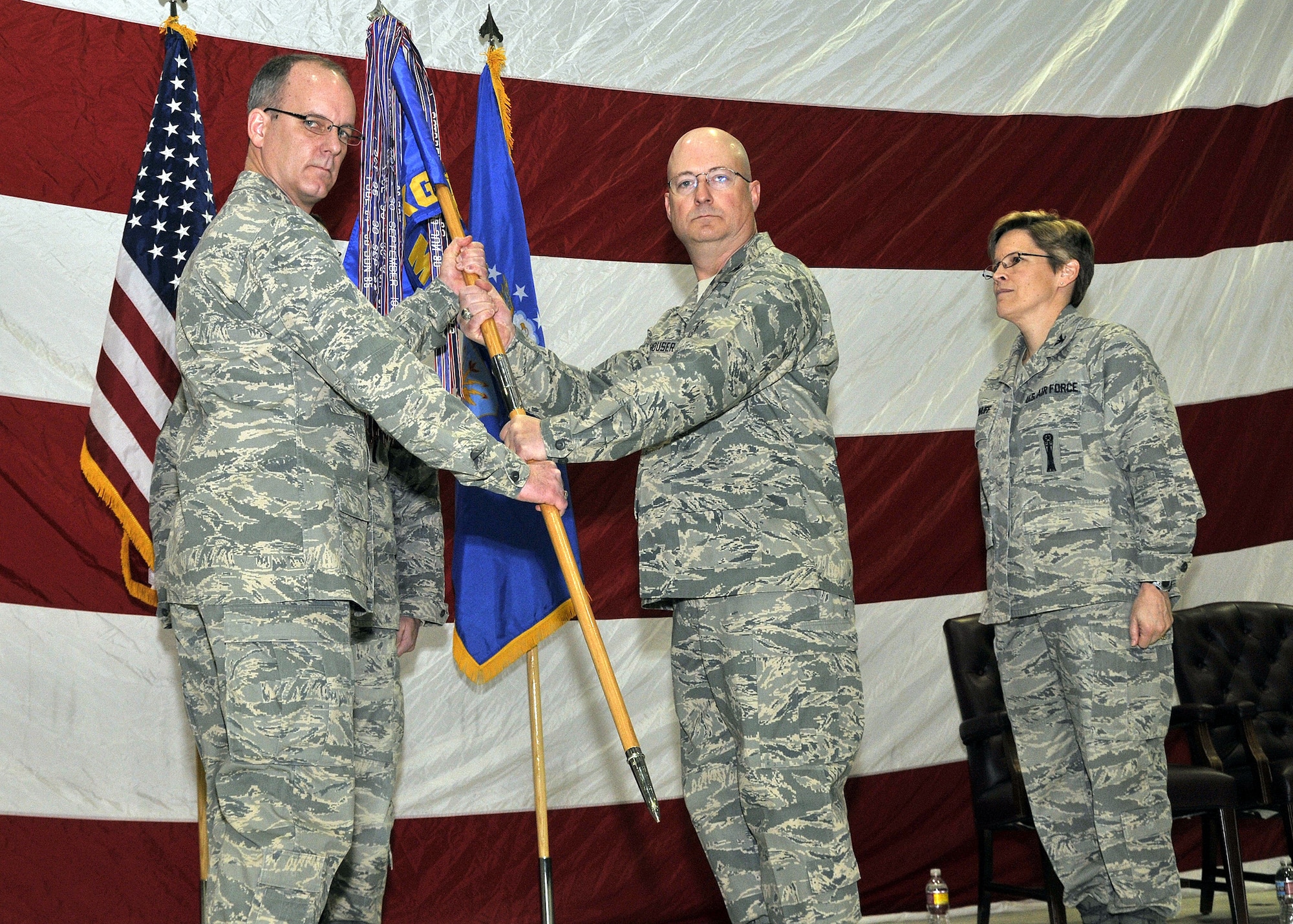 Col. Michael Fortney, 341st Missile Wing commander, passes the 341st Maintenance Group guidon to Col. Jeffrey Frankhouser March 6 during a change of command ceremony in the 3-Bay Hanger. Outgoing 341st MXG Commander Col. Deborah Kirkhuff looks on. (U.S. Air Force photo/John Turner)