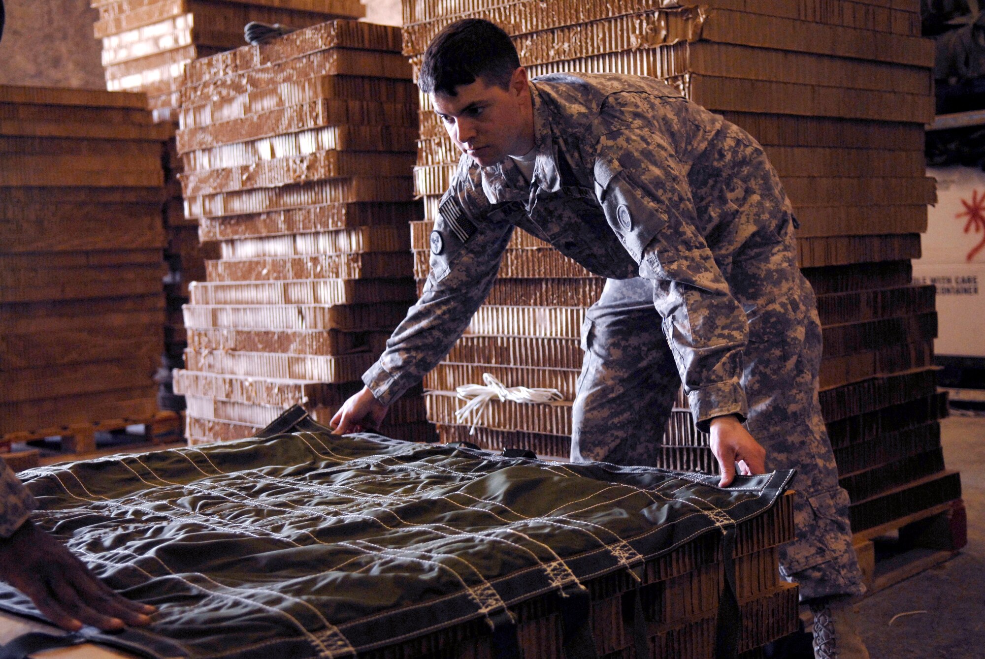 U.S. Army Sergeant David Kaspar, 824th Quartermaster Company Detachment 7 Rigger, places the container cover down before the commodity bundle is placed on top to be wrapped and packed for an air drop to a base in the U.S. Central Command's area of responsibility (AOR), Mar. 9, 2009, at an undisclosed location in Southwest Asia.  Shipments of food, ammunition, and fuel prepared by the riggers can be destined for any coalition forces on the ground across the AOR.  Sgt. Kaspar hails from Fort Lee, Va. and is deployed from Fort Bragg, N.C. in support of Operations Iraqi and Enduring Freedom and Combined Joint Task Force - Horn of Africa.  (U.S. Air Force Photo by Senior Airman Andrew Satran/Released)