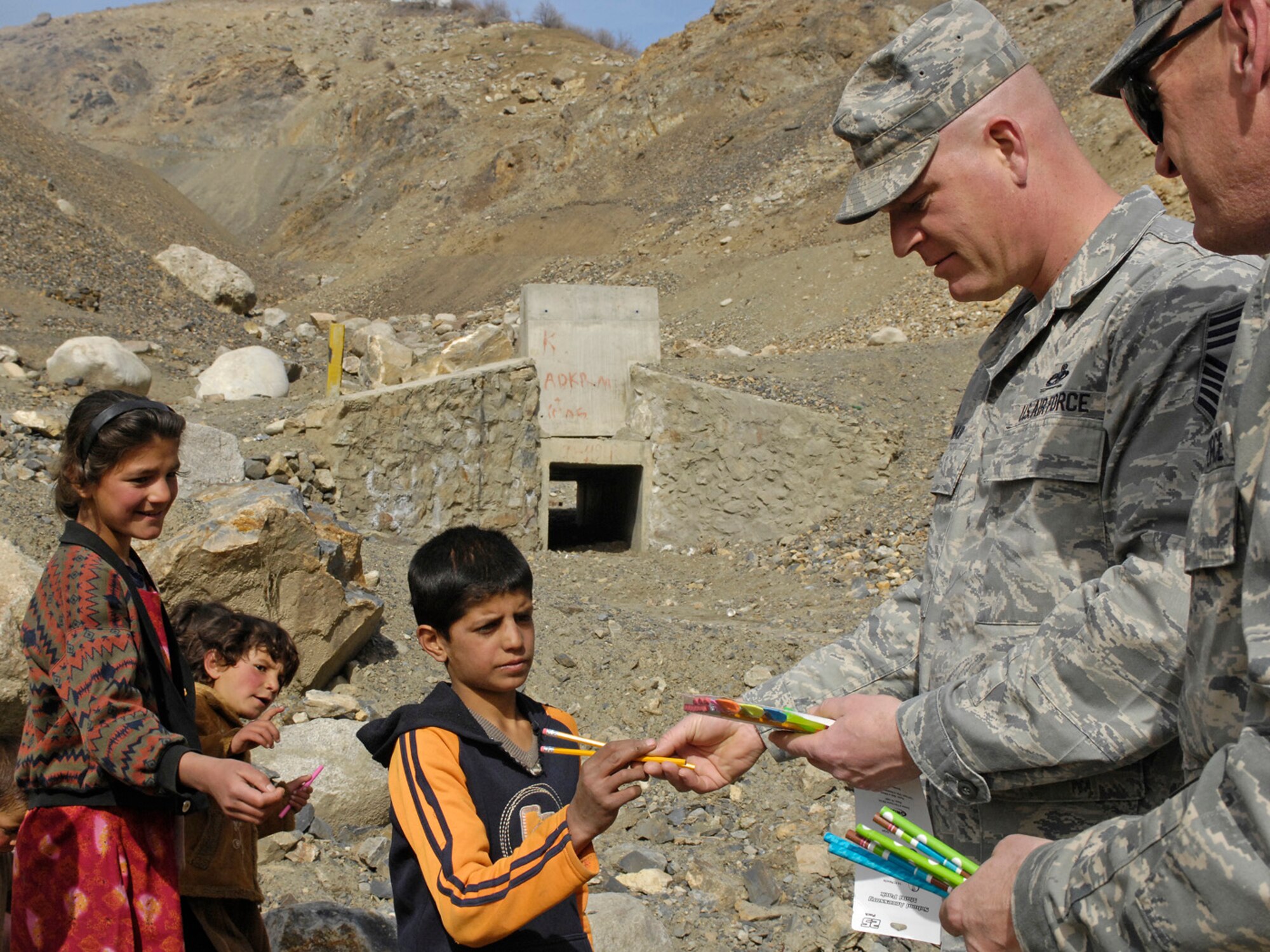 Chief Master Sgt. John Blair, 755th Air Expeditionary Group command chief master sergeant, and Master Sgt. Lance Turner, 755th AEG first sergeant, hand out pencils and pens to children during a site visit March 8 to Forward Operating Base Lion and the neighborhoods of Rokha. The two, also accompanied by Col. James Reed, 755th AEG commander, and 455th Air Expeditionary Wing leadership, visited the Abdawa micro hydro power plant site, Pyawusht health clinic and several other construction and repair projects in the Rokha district of Panjshir province, Afghanistan. (U.S. Air Force photo by Staff Sgt. Jason Lake)
