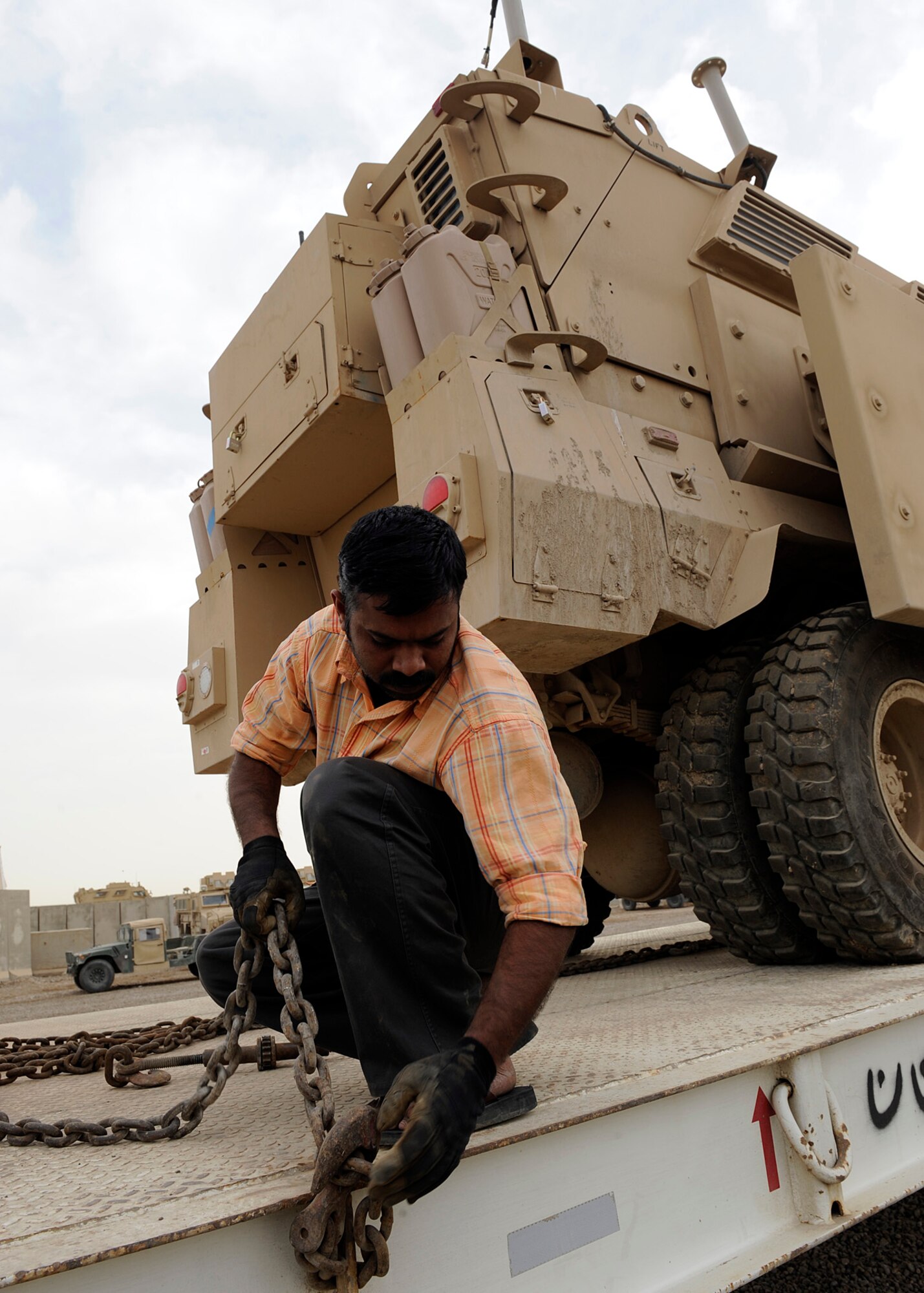 An Iraqi contractor makes sure the chains are connected to the semi truck so that he can prep the mine resistant ambush protected vehicle at Camp Liberty, Iraq on Feb. 27, 2009. The MRAP is being secured onto the bed of the truck so that it can be transported in a convoy.  One of the redistribution property assistance team’s primary duties is to issue military vehicles out to the Army for either combat or support.  The personnel at the yard have been able to more than $1 billion worth of equipment in their six month deployments.  (US Air Force Photo By: Senior Airman Jacqueline Romero)
