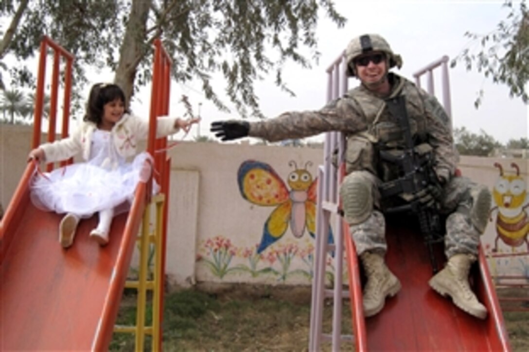 U.S. Army Sgt. Stephen Covell, a native of Pacific Grove, Calif., along with an Iraqi girl go down a slide at the playground during the reopening of the Al-Moutasam Kindergarten March 3, 2009, in the Rusafa district of eastern Baghdad. Covell is a medic assigned to Headquarters and Headquarters Troop, 5th Squadron, 73rd Cavalry Regiment, 3rd Brigade Combat Team, 82nd Airborne Division, Multi-National Division-Baghdad.                         