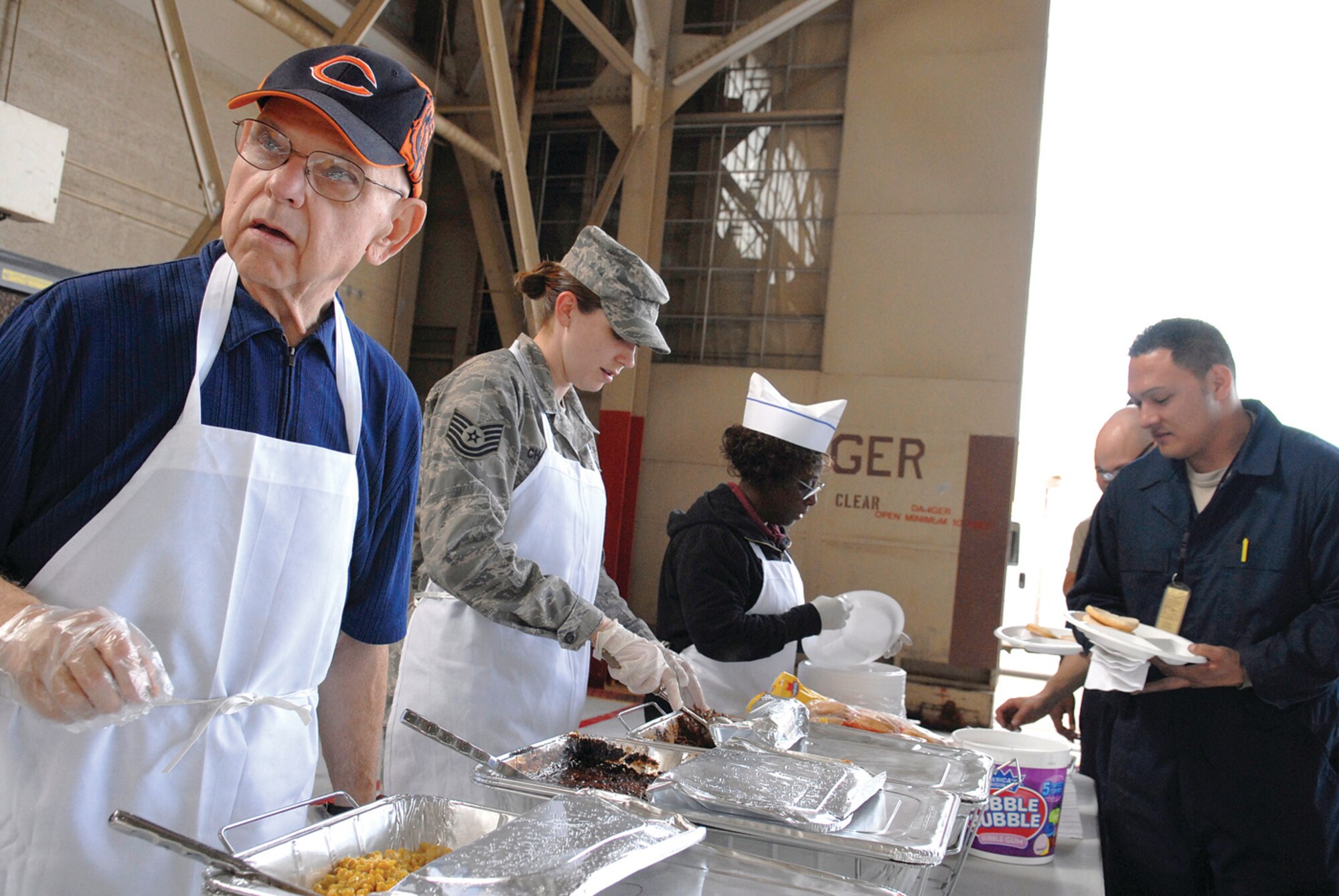 Carl Main, a missionary with Cadence International and Luke chapel volunteer; Tech. Sgt. Sadie Chambers, 56th Fighter Wing chaplain assistant; and Sandy Harris, a volunteer who works with the Protestant Women of the Chapel, work together on the serving line at the chapel-sponsored event Flightline Feast on March 5 in Hangar 914. On average, 150 to 250 Airmen attend the Flightline Feast every month, which rotates between a lunch meal for the day shift workers one month and a dinner for the swing shift workers the alternating month.(Deborah Silliman-Wolfe)