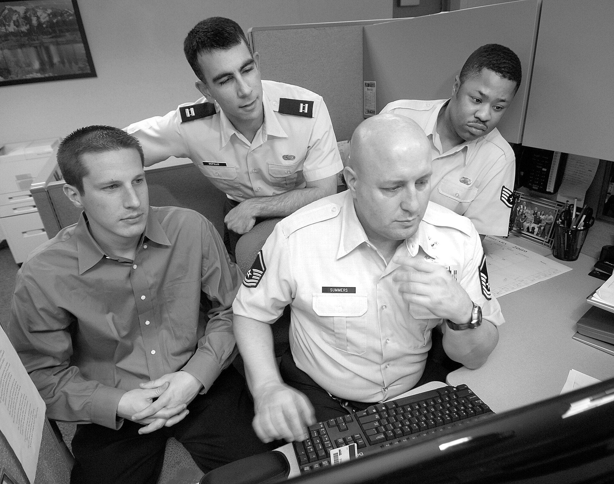 Members of the 5th Manpower Requirements Squadron review a description of functional tasks, known to them as a POD or Process Oriented Description.  “C” Flight team lead Master Sgt. Michael Summers drives the computer work with flight members, from left, Sam Packard, industrial engineer; Capt. Fernando Defillo, flight OIC; and analyst Staff Sgt. Meldon Street. (Air Force photo/Margo Wright) 