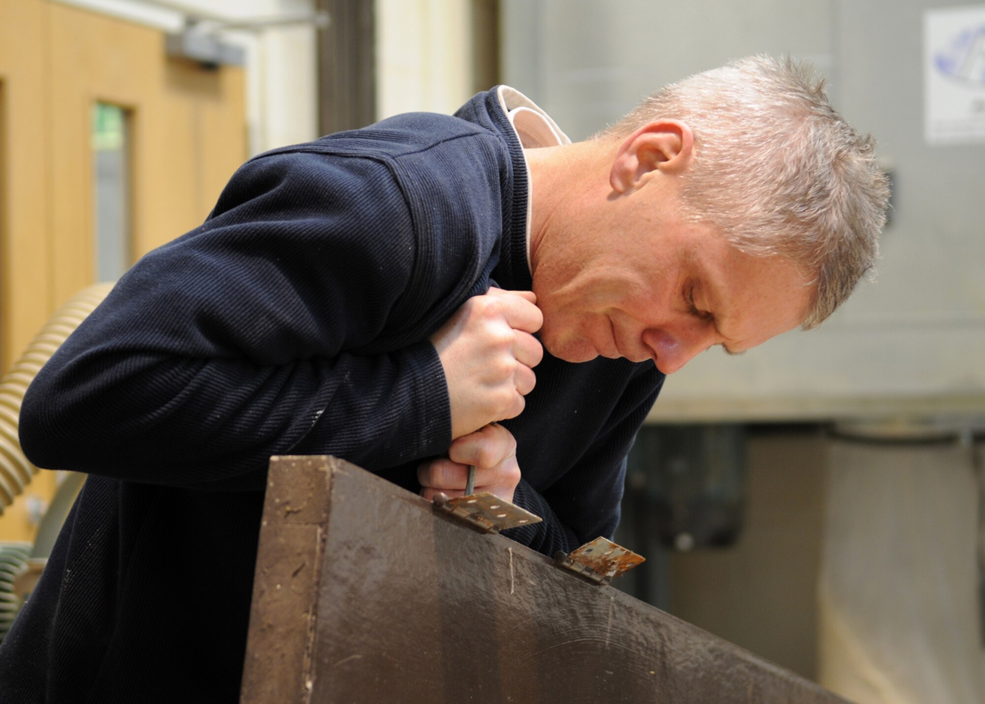 Ministry of Defence worker Philip Bower, a 100th Civil Engineering Squadron maintenance carpenter, fights to remove stuck screws from an old door hinge as a March 3, 2009, at RAF Mildenhall, England. Mr. Bower removes all the old hinges and hardware prior to repairing the broken door. (U.S. Air Force photo by Staff Sgt. Jerry Fleshman)