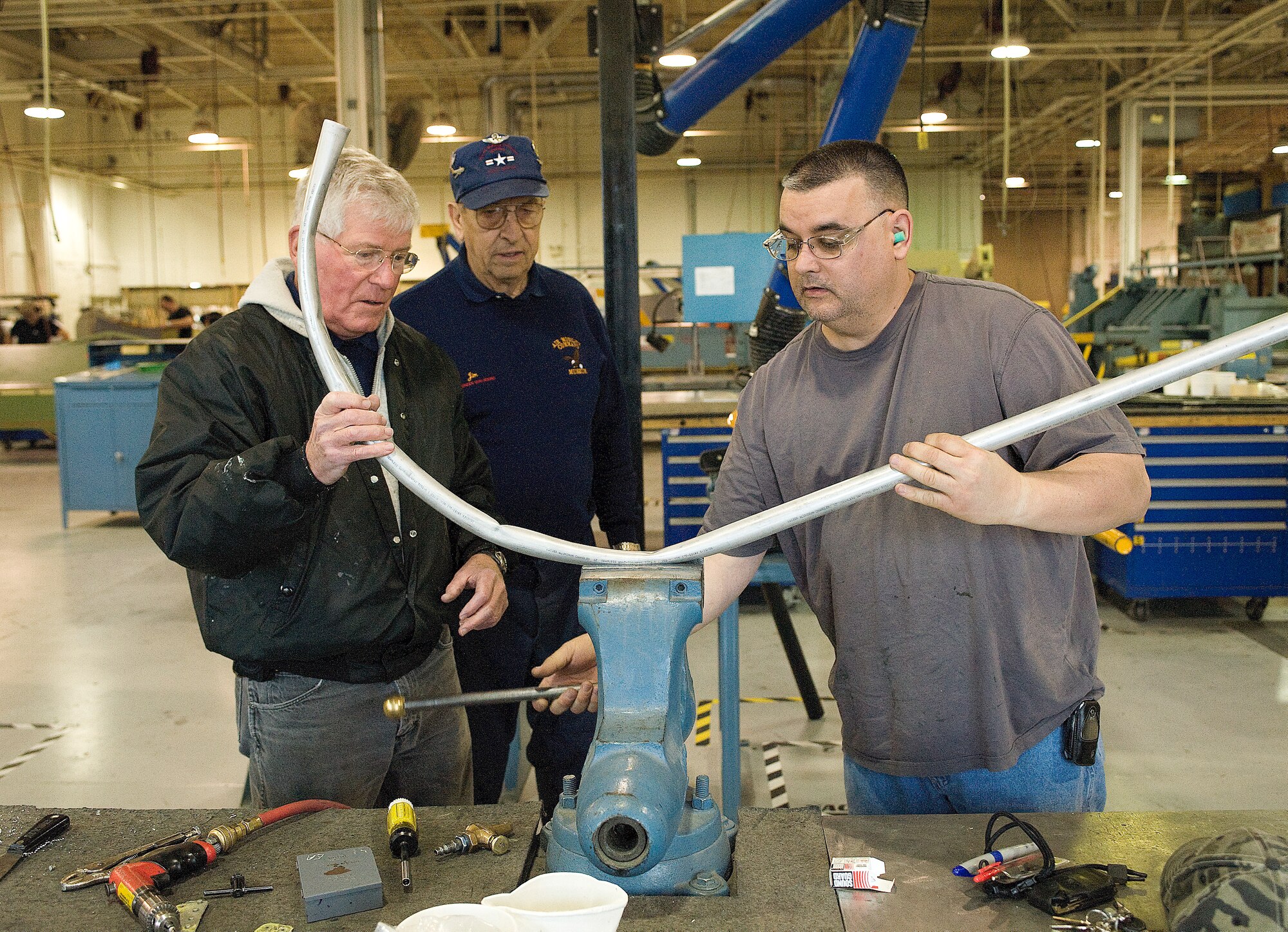 (From right) Ed Pagan, 436th Maintenance Squadron, helps Air Mobility Command Museum volunteers Jim Nolan and Sandy Sandstrom, bend a piece of metal for a simulated ignition coil for an aircraft.  Mr. Sandstrom and Mr. Nolan are part of a group of volunteers who repair aircraft for display at the AMC Museum.  (U.S. Air Force photo/Jason Minto)