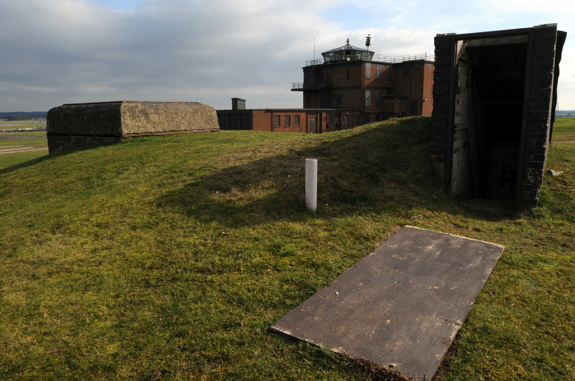 Two structures from two different eras sit next to each other near the RAF Lakenheath flight line Feb. 27, 2009. The command bunker in the foreground was used by commanders during World War II to defend the airfield against German Paratroopers. The control tower in the background is a relic of the Cold War Era and was used from 1948 through 1992, it’s scheduled to be demolished. (U.S. Air Force photo by Staff Sgt. Nathan Gallahan)