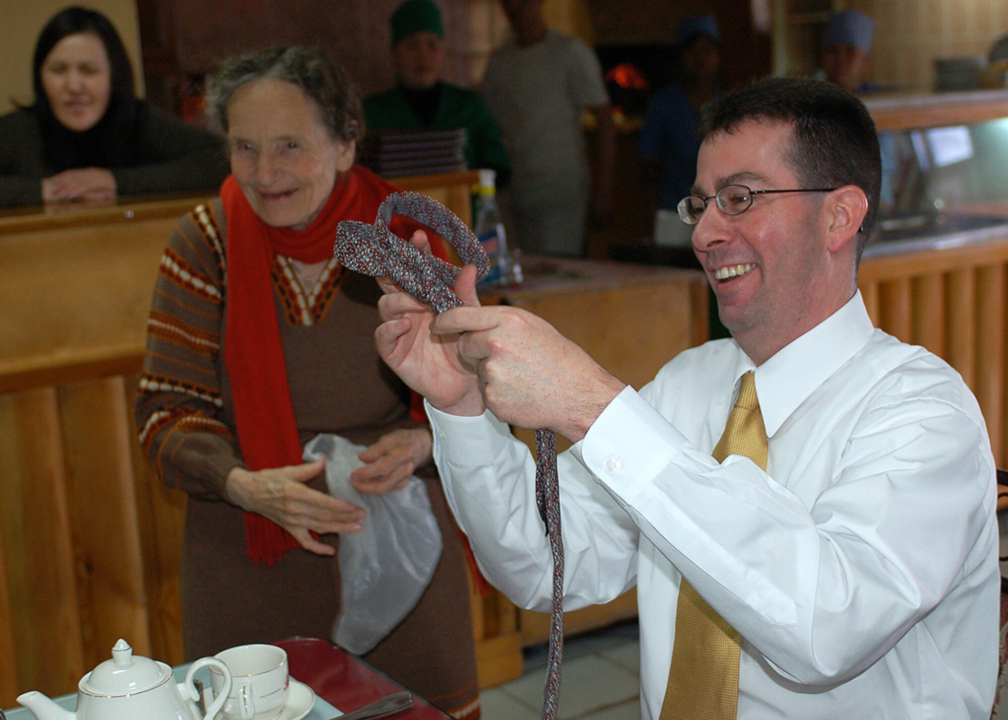 Chief Master Sgt. Richard Coyle admires his new tie that Vera Wolf gave to him during a lunch visit with Manas Air Base Outreach Society members March 9 at a Turkish restaurant in Bishkek, Kyrgyzstan. Vera is known as a Babushka, or elderly woman, in Russian and Kyrgyz cultures. The 78-year-old woman has no family and was ?adopted,? along with two other elderly women, by MABOS through the Babushka Adoption Foundation, a local non-governmental organization. Each lady?s monthly income averages about 700 som or around $20 per month. Every month, volunteers from Manas join the ladies for lunch to share companionship, a little financial support and a small supply of groceries. Chief Coyle is the superintendent of the 376th Expeditionary Medical Group and is deployed from the 355th Medical Support Squadron at Davis-Monthan Air Force Base, Ariz. (U.S. Air Force photo/Tech. Sgt. Elizabeth Weinberg)