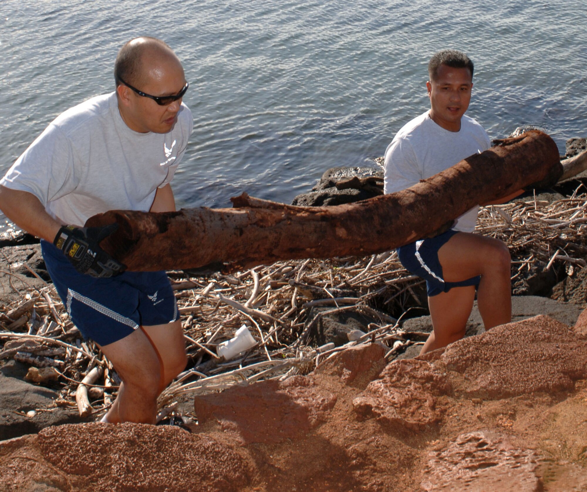 Lt. Col. Lamberto Braza (left) and Col. Amando Gavino heave a driftwood log from the rocky shoreline March 13 at Ala Moana Beach Park in Honolulu. The Airmen volunteered for the beach cleanup as part of 13th Air Force's Jungle Day, a tradition for the unit that occurs every Friday the 13th. (U.S. Air Force photo/Oscar A. Hernandez) 
