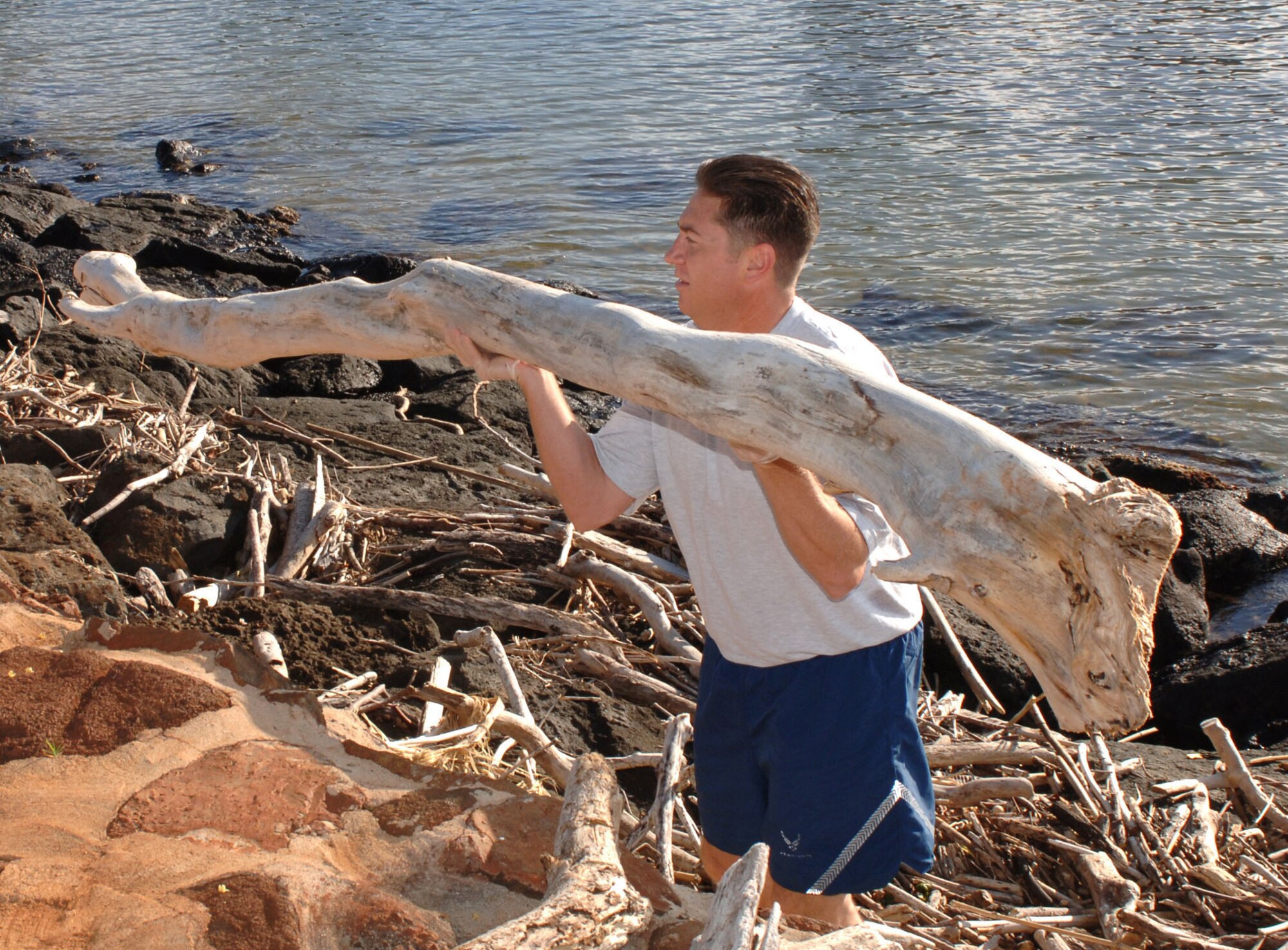 Senior Master Sgt. Terry Rishty heaves a driftwood log as he cleans trash and debris from the rocky shoreline March 13 along Ala Moana Beach Park in Honolulu. Airmen from 13th Air Force at Hickam Air Force Base volunteered for the beach cleanup as part of the organization's Jungle Day, a tradition for the unit that occurs every Friday the 13th. (U.S. Air Force photo/Oscar A. Hernandez) 
