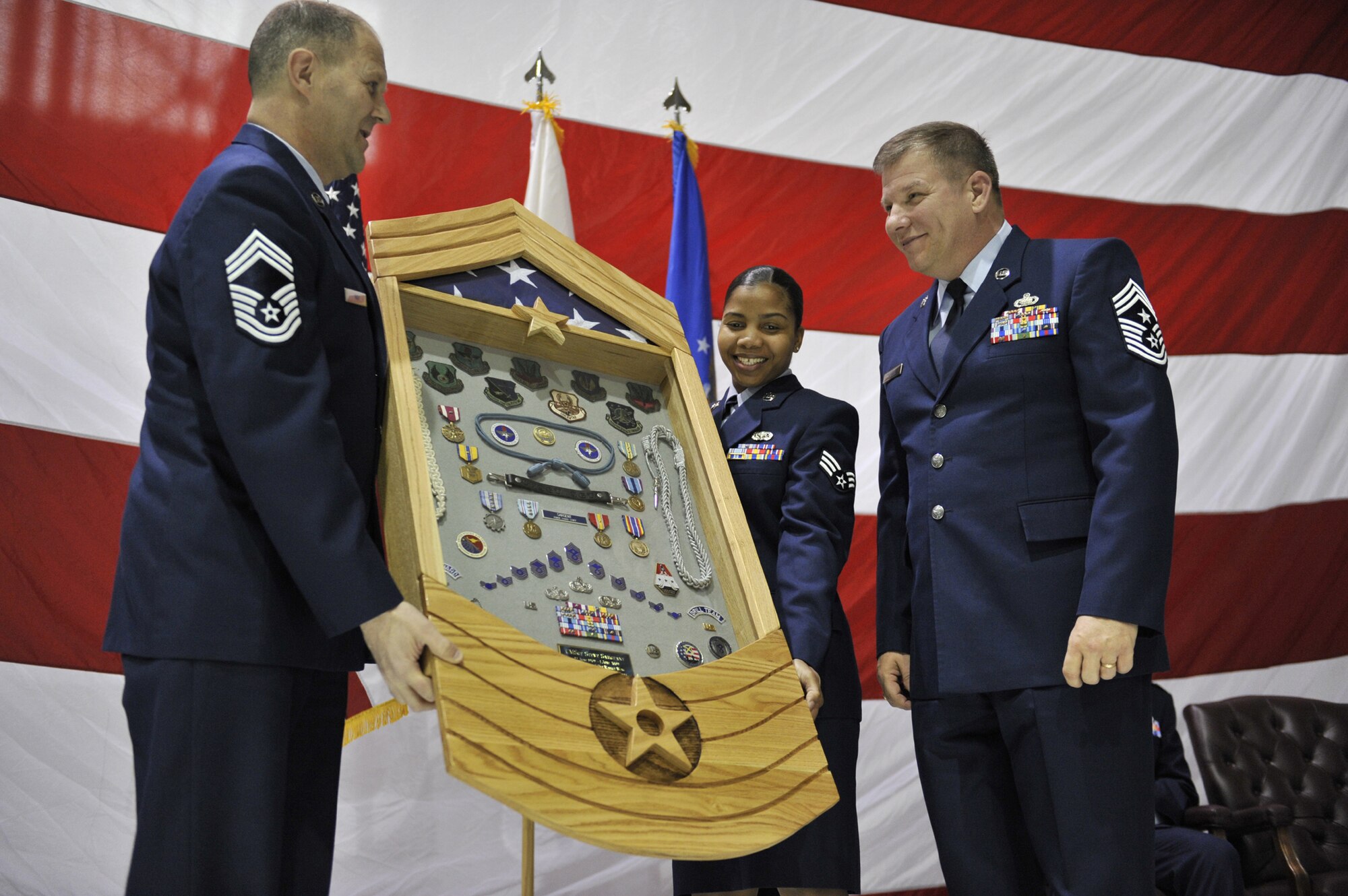 Chief Master Sgt. Don May, 341st Operations Group superintendent, and Senior Airman Chanice Reid, 341st OG senior missile chef, present Chief Master Sgt. Steve Sargent, 341st Missile Wing command chief, with a shadow box during his retirement ceremony March 13 in the Three Bay Hangar. (U.S. Air Force photo/John Turner)