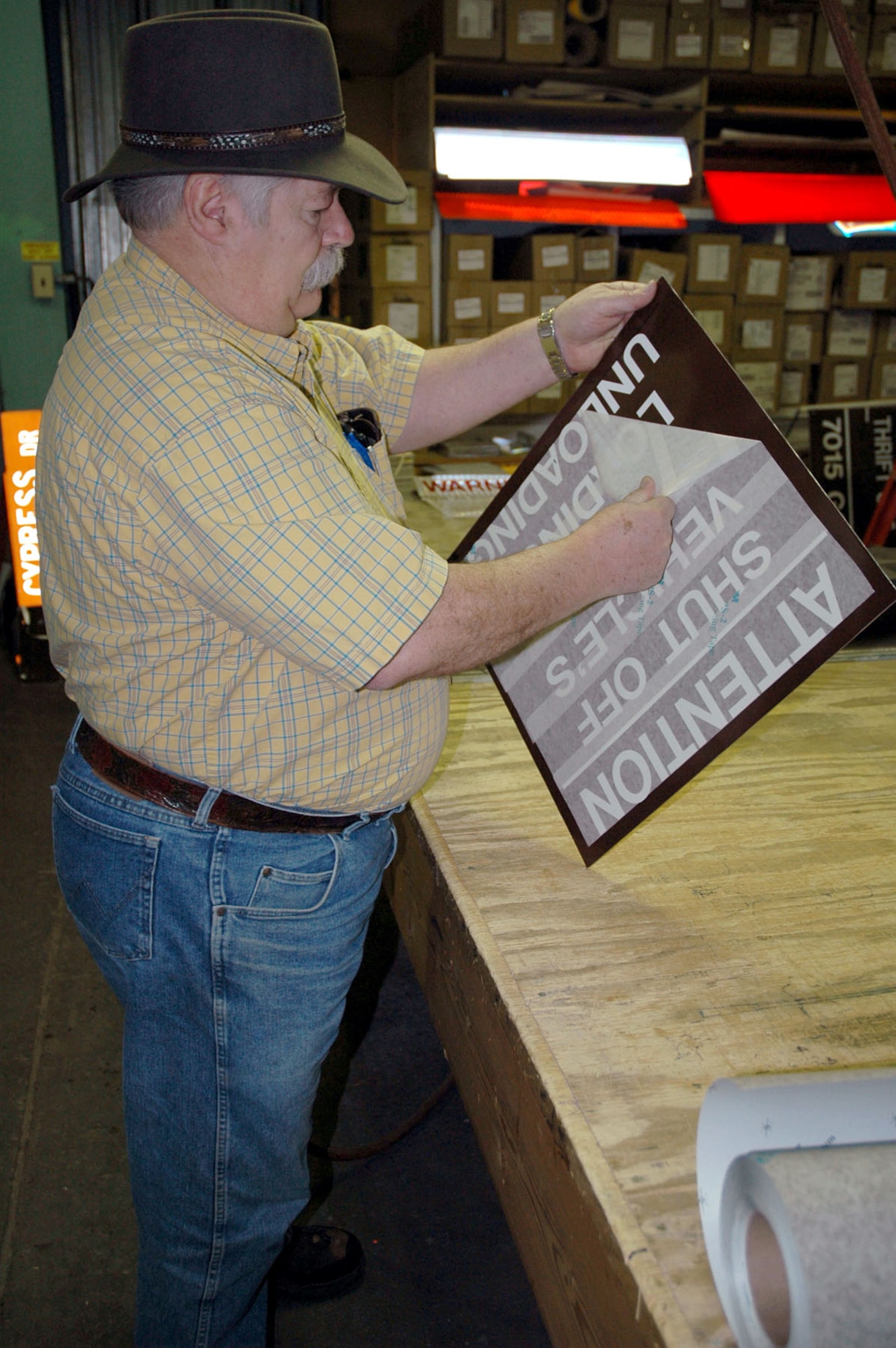 Cliff Holmes, 341st Civil Engineer Squadron sign craftsman, peels a paper backing off vinyl lettering March 11 at the base sign shop. (U.S. Air Force photo/Senior Airman Dillon White)