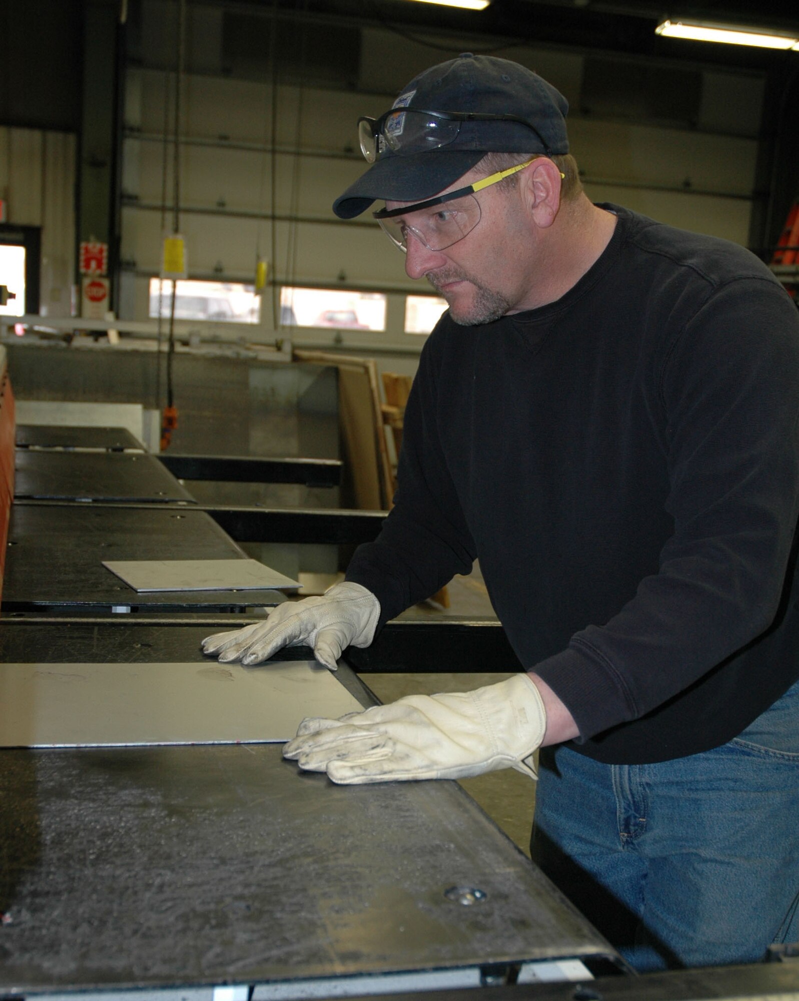 Mark Boser, 341st Civil Engineer Squadron welder, pushes a sheet of anodized aluminum into a cutting press  that shears sign blanks to their appropriate lengths at the metal shop March 16. (U.S. Air Force photo/Senior Airman Dillon White)