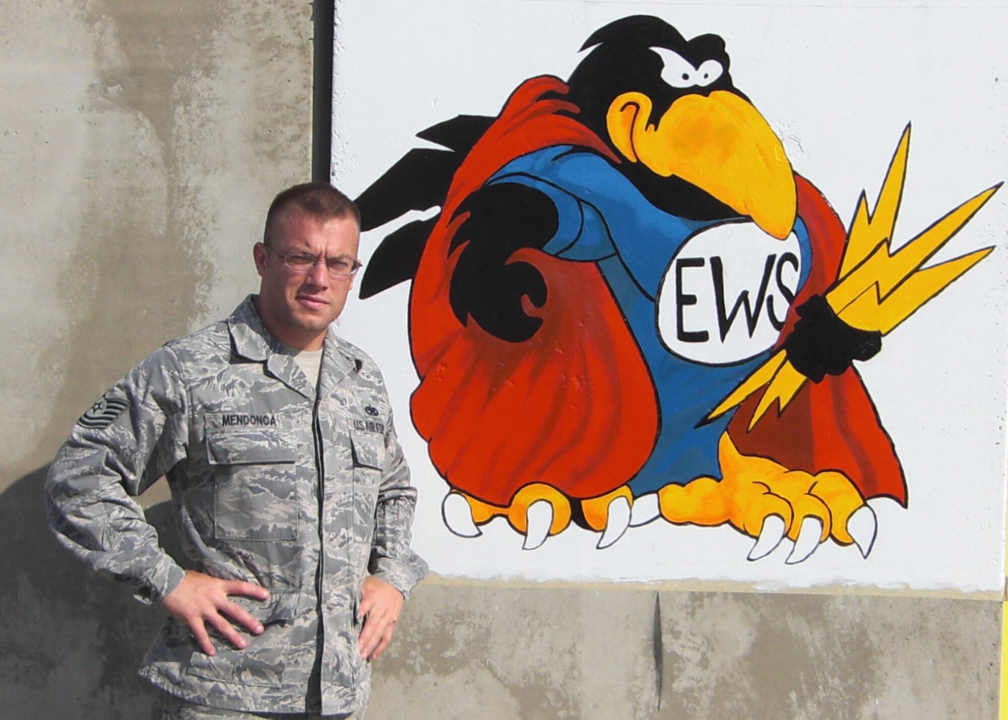 JOINT BASE BALAD, Iraq -- Tech. Sgt. Christopher Mendonca, 35th Maintenance Squadron electronic warfare systems section producer, stands in front of an EWS crow painting Nov. 24, 2008. Although he was deployed as the EWS NCO in charge, Sergeant Mendonca spent nearly 300 volunteering at the base hospital and helping injured patients. (Courtesy photo)
