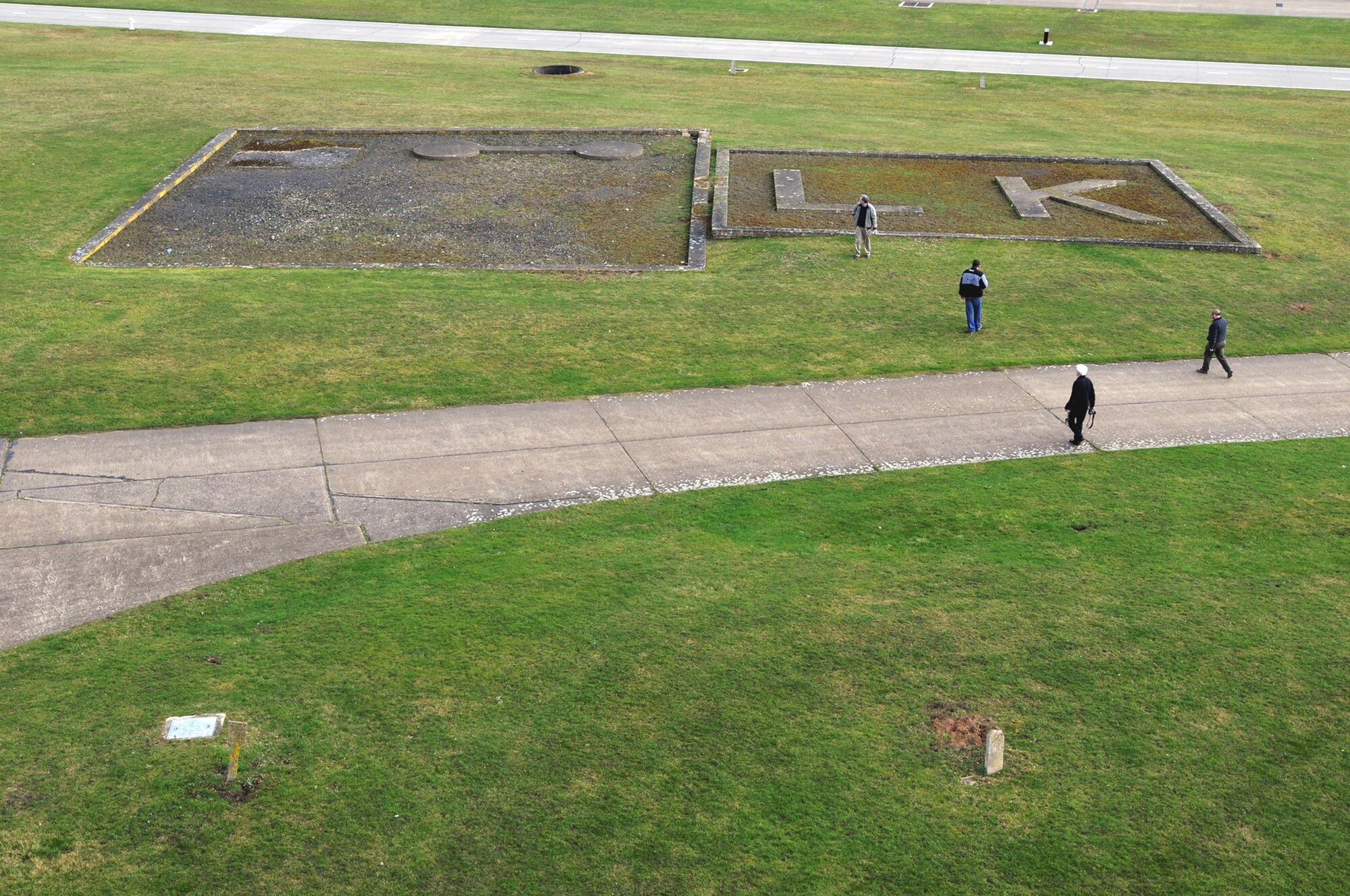 A team of historians walks out to World War II airfield marker at Royal Air Force Lakenheath, England, Feb. 27. The marker sits in front of an old air traffic control tower which is scheduled to be demolished. Although the team was visiting to document the tower, they took the opportunity to study other historical structures as well. During the war, when hundreds of aircraft were flying over the airfields of East Anglia, pilots could look down and see these markers, "LK" represents RAF Lakenheath, and they're used to be a big rotating sign to the left of it that Airmen could turn to tell pilots which runways to land on. (U.S. Air Force photo/Staff Sgt. Nathan Gallahan)