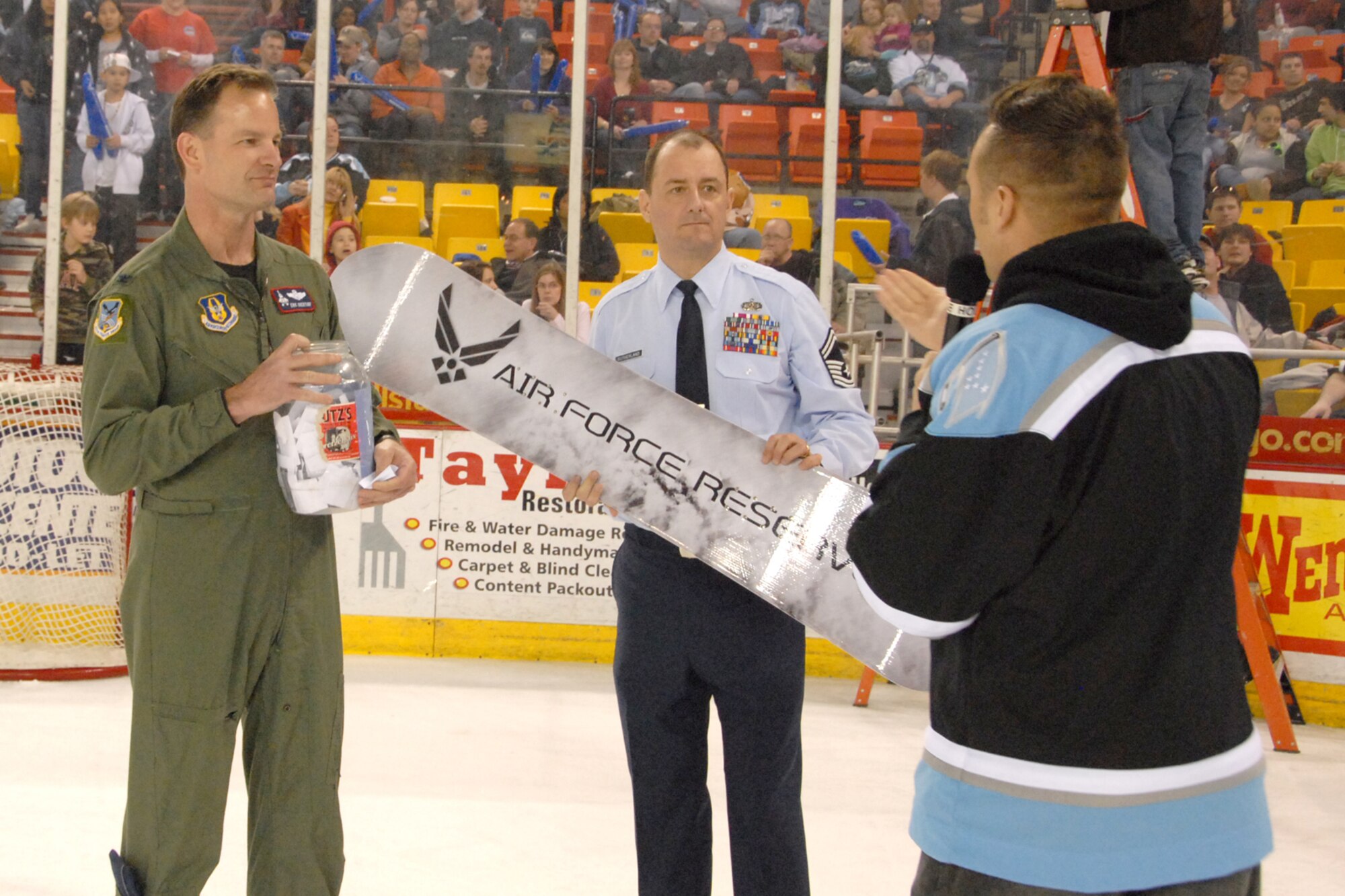 ANCHORAGE, Alaska -- Colonel Eric Overturf, 477th Fighter Group Commander, and Senior Master Sgt. Gerald Sutherland, Air Force Reserve Recruiting Services, draws a name for the Air Force Reserve Snowboard raffle during the Alaska Aces hockey game March 14.  The Alaska Aces sponsored a night full of 477 FG events.  They displayed videos and photos on the Aces jumbo screen and gave free tickets to 477 FG Reservists.  The 477th Fighter Group is Air Force Reserve Command's first F-22A Raptor unit and the first Reserve flying unit based in the Pacific theater of operations. (U.S. Air Force Photo by Tech. Sgt. Rhiannon Willard)