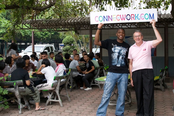 Cpl. Eric McIntyre, a ground supply property noncommissioned-officer-in-charge with Marine Aircraft Group 12 and creator of Connecwork.com, holds a sign with Richard Bosson, an overseas English teacher at Boonwattana secondary school, announcing the official commencment of the new networking website, Connecwork.com during a visit to Boonwattana secondary school in Korat, Thailand March 18. Connecwork.com is an educational social networking website originally created to keep the students of Boonwattana secondary school connected with American service members around the world.