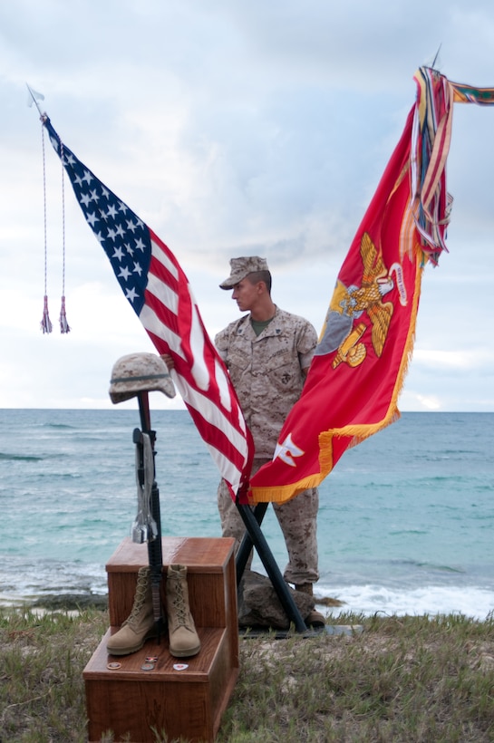 Sgt. Dustin Ramirez, tech controller, 3rd Marine Regiment, stands with the colors of the unit and a battlefield cross during a morning memorial ceremony June 4. Ramirez was one of more than 1,200 of the regiment who stood in formation and as the names of 114 fallen service members were read aloud at Fort Hase Beach.