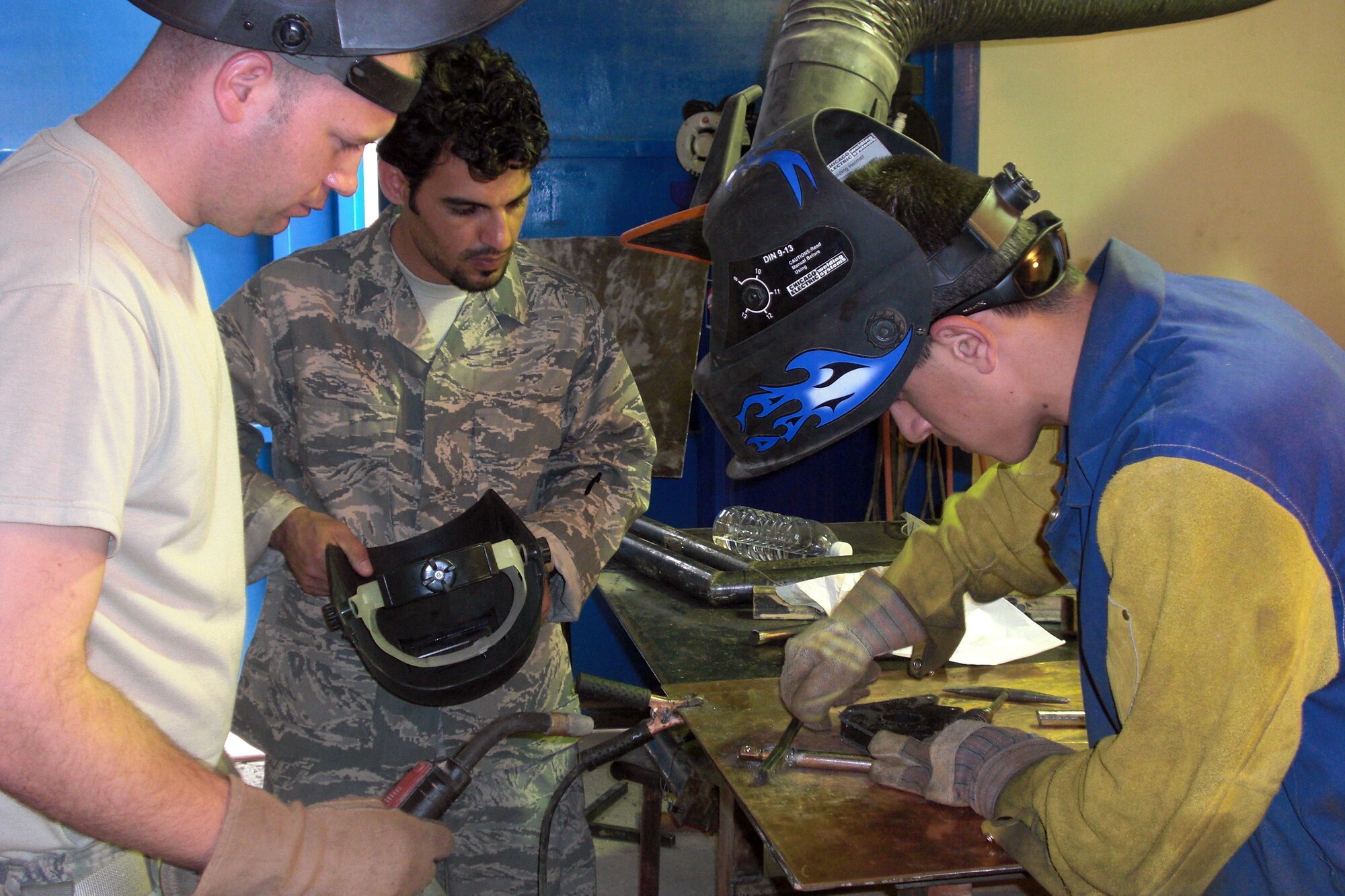 Tech. Sgt. Bobby McKenzie, left, 321st Air Expeditionary Advisory Squadron aircraft structural maintenance advisor, looks on with the help of an Iraqi interpreter while an Iraqi machinist fabricates a torque tool for C-130 main landing gear brakes at Camp Taji. Sergeant McKenzie took three Iraqi air force members to Camp Taji, Iraq to help better cross utilize their resources and also fix an IraqC-130s. Sergeant McKenzie is deployed from Little Rock AFB, Ark., and is a native of Manchester, Tenn.  (Courtesy photo)
