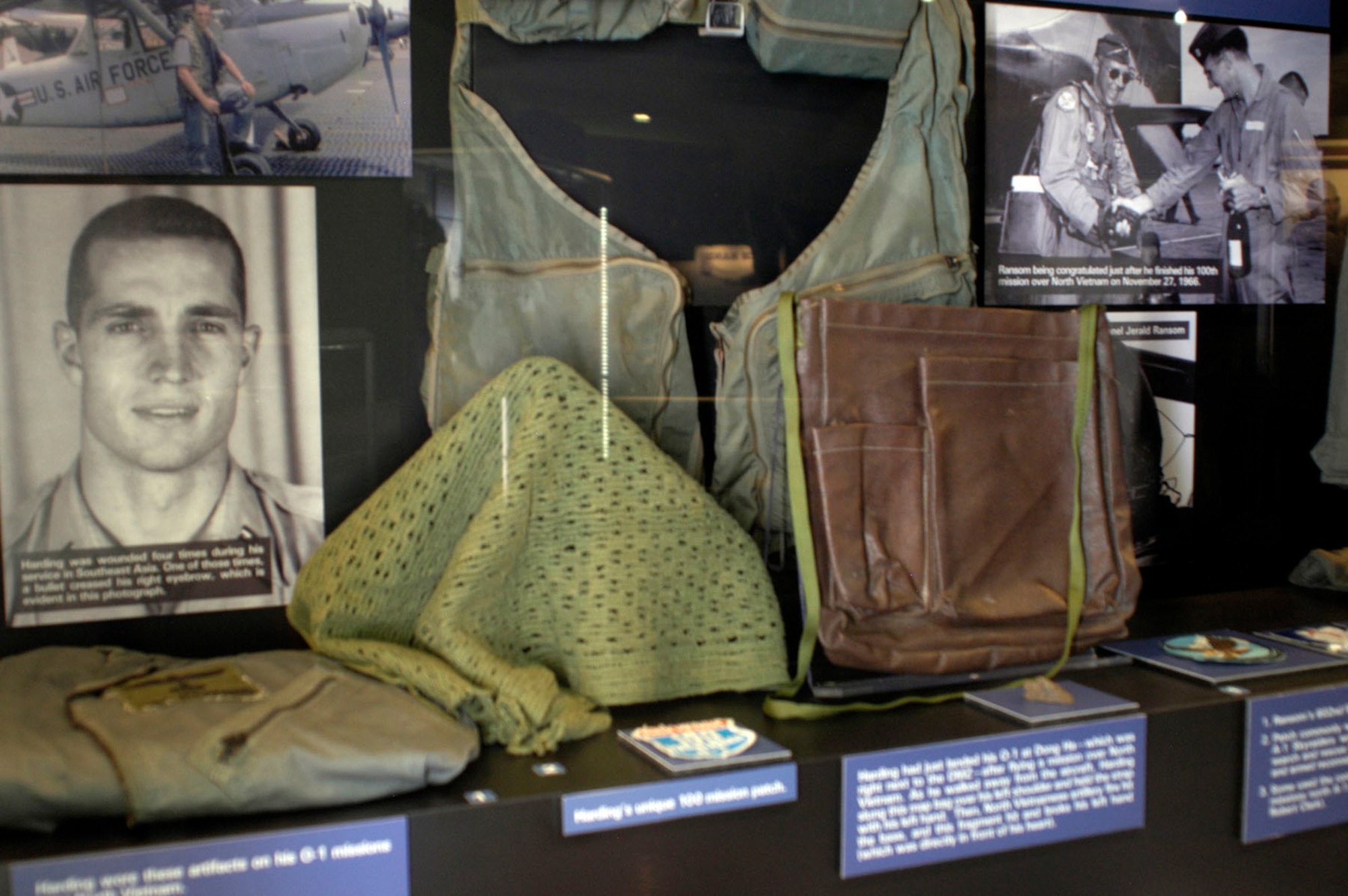 DAYTON, Ohio - Flight suit, scarf, and survival chaps worn by Maj. James Harding on his O-1 missions over North Vietnam. Harding obtained the scarf while attached to Australian troops as a ground air liaison officer. Harding had just landed his O-1 at Dong Ha—which was right next to the DMZ—after flying a mission over North Vietnam. As he walked away from the aircraft, Harding slung this map bag over his left shoulder and held the strap with his left hand. Then, North Vietnamese artillery fire hit the base, and this fragment hit and broke his left hand (which was directly in front of his heart). Harding’s unique 100 mission patch. (U.S. Air Force photo)