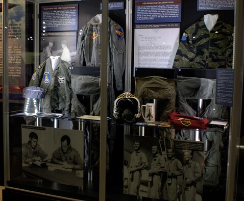DAYTON, Ohio - In this case from the 100 Missions Up North exhibit in the museum's Southeast Asia War Gallery are Capt. Ben Bowthorpe’s flight suit and g-suit worn during his 100-mission tour. Later pilots flying over the North wore “sanitized” flight suits with no rank or unit insignia. Bowthorpe wore this cap from the briefing room to the airplane, stored it in his g-suit pocket before takeoff, and put it back on after landing. Also shown is Bowthorpe’s flight jacket. On the right is Capt. Bruce Holmes' tiger suit, Capt. Richard Ely's helmet and oxygen mask wore during his 100-mission tour (Ely used this air navigation computer during his 100 missions) and Ely’s F-105 100 mission patch. Ely and the other three were the first to wear this symbolic patch. Display also includes patch for the 355th Fighter Wing at Takhli RTAFB, Capt. Ely’s Red River Valley Fighter Pilots stein, and an enemy bullet and fragment dug out of the cockpit of his F-105 after one of his missions. Additionally, a g-suit and kneeboard used by Capt. William May on his 100-mission tour, May’s party suit with 100-mission patch and a g-suit worn by Capt. William Ramage on his 100-mission tour. (U.S. Air Force photo)