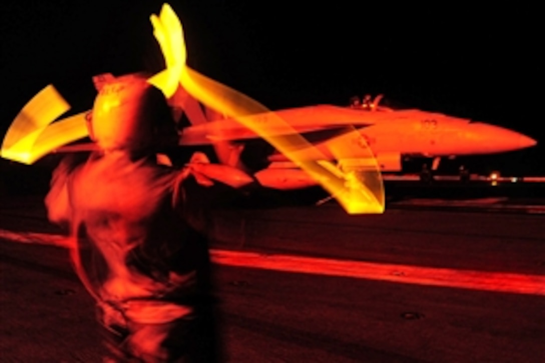 A U.S. Navy aviation boatswain's mate directs an F/A-18F Super Hornet strike fighter  to a catapult during flight operations aboard the aircraft carrier USS Theodore Roosevelt in the Gulf of Oman, March 19, 2009.