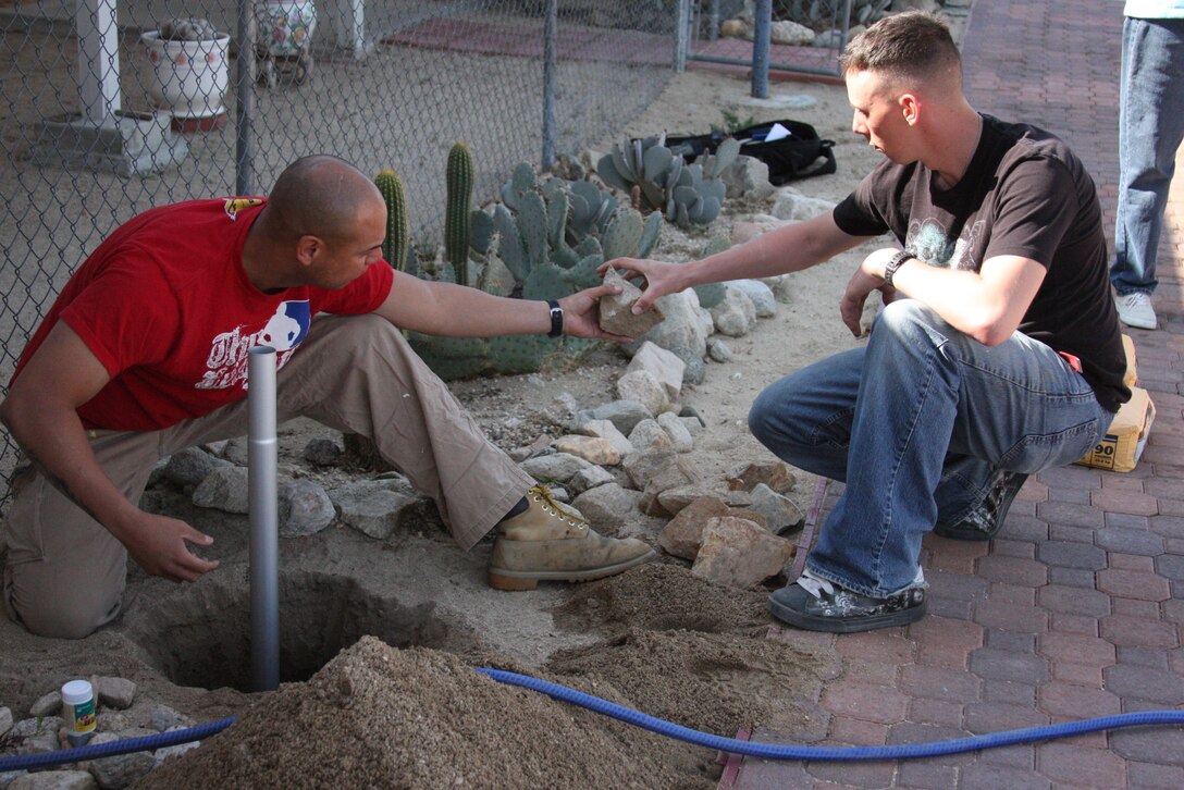 Sgt. Rolando Delacruz (left), a combat engineer with Headquarters and Service Company, 3rd Combat Engineers Battalion, and Lance Cpl. Chris Nichols, supply administration and operations specialist with H&S Company, 3rd CEB, create a base for a flagpole outside of Korean War veteran Richard N. Blasongame’s home in Joshua Tree, Calif., March 25.