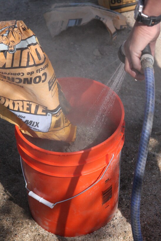 Marines with 3rd Combat Engineers Battalion mix a bucket of cement to create a base for a new flagpole being built outside the home of Korean War veteran Richard N. Blasongame March 25.