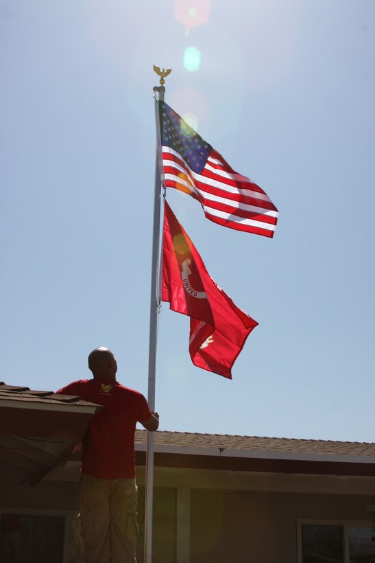 Sgt. Rolando Delacruz, a combat engineer with Headquarters and Service Company, 3rd Combat Engineers Battalion, finishes the final touches of flying a new pair of Marine Corps and American flags on a new flagpole built outside the home of Korean War veteran Richard N. Blasongame, March 25.