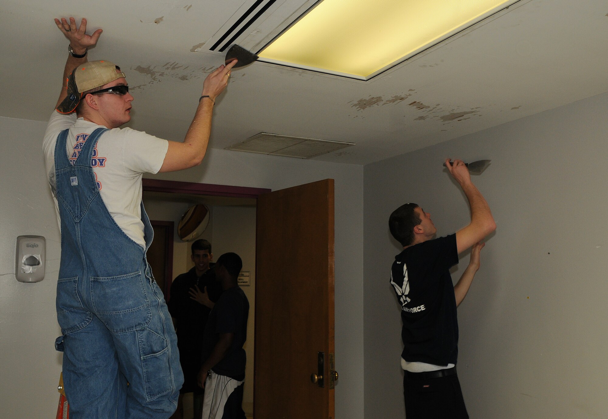 Senior Airmen Palmer Durrence and William Enterkine, 11th Logistics Readiness Squadron, scrape paint from a ceiling in a treatment room during a painting project March 21 at Saint Elizabeth's Hospital, Washington. National Capital Region Airmen volunteered their weekend to help hospital staff members paint high-traffic areas used daily by patients and staff who are part of their treatment mall – the recovery program that patients attend Monday through Friday to prepare to return to the community. (U.S. Air Force Photo by Senior Airman Marleah Miller)