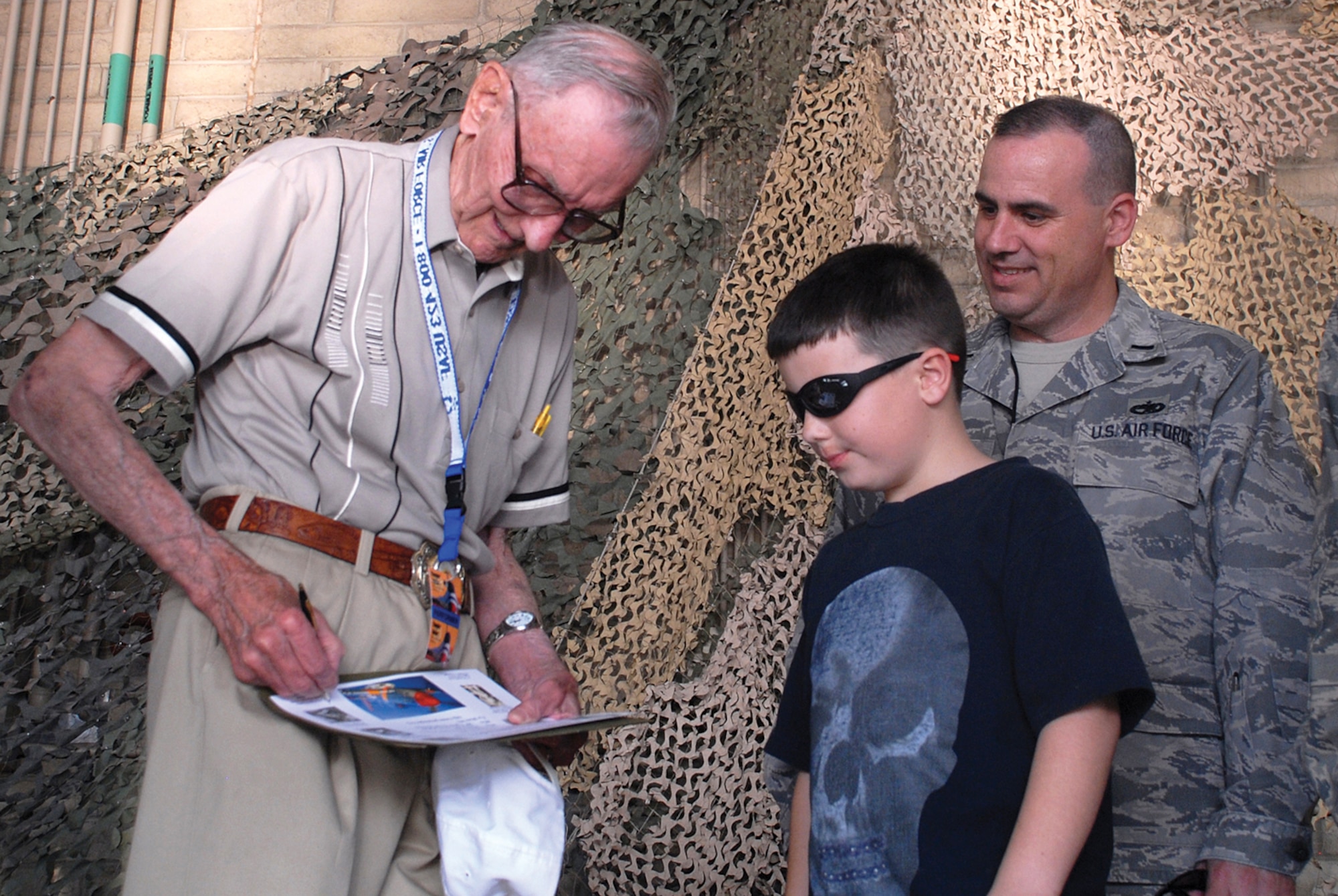 Retired U.S. Air Force Major Ralph Wandrey autographs a poster for Ransom Trueman, the son of 1st Lt. Frederick Trueman, commander of the 56th Equipment Maintenance Squadron Fabrication Flight, during the Wing Warrior Call held in Hangar 431 before the 2009 Luke Days kick off party, March 20. (U.S. Air Force photo/Airman 1st Class Tracie Forte)