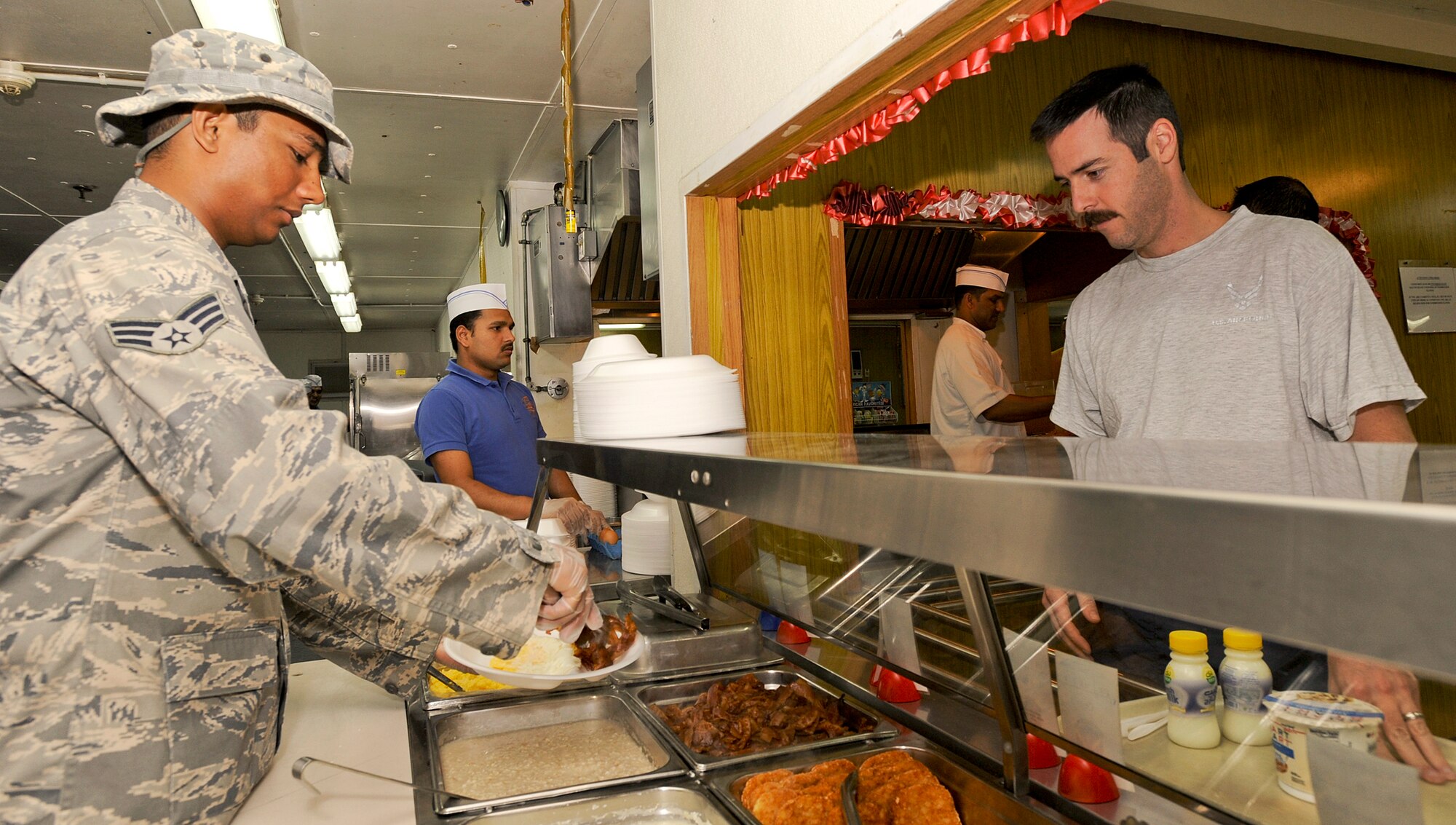 Senior Airman Cecil D'Souza serves Maj. Corbit Bufton breakfast March 23 at an air base in Southwest Asia. Military members working in the dining facilities aid local contract workers in serving and cooking the food during peak meal hours. Airman D'Souza is a services journeyman with the 379th Expeditionary Force Support Squadron. He is a native of Virginia and is deployed from McChord Air Force Base, Wash. Major Bufton is a C-17 Globemaster III pilot with the 816th Expeditionary Airlift Squadron. (U.S. Air Force photo/Staff Sgt. Joshua Garcia) 
