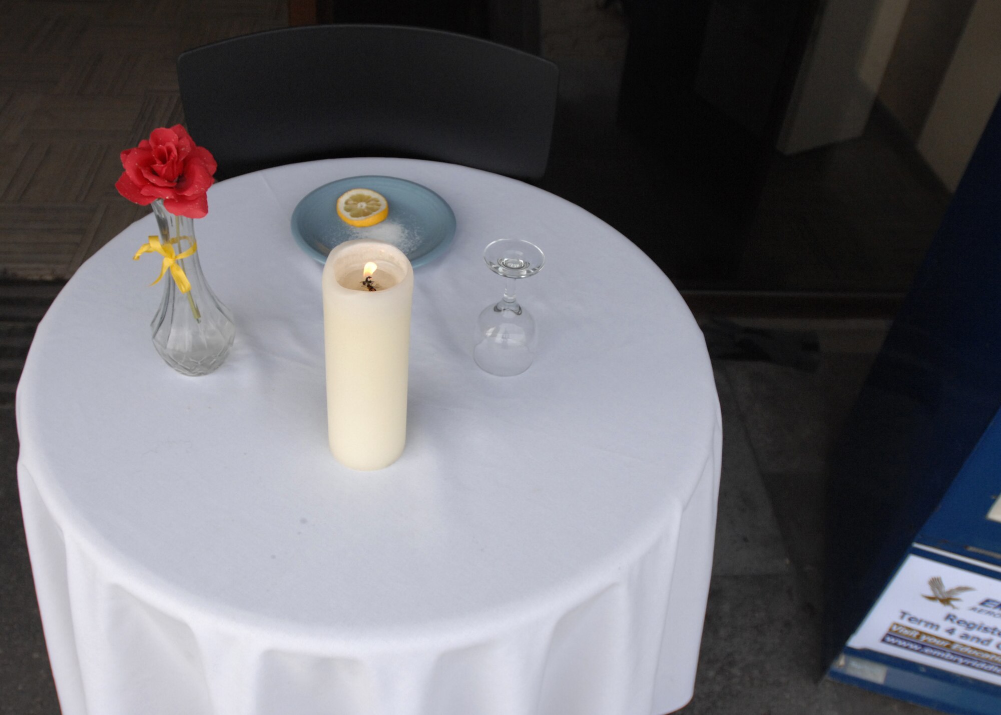 SPANGDAHLEM AIR BASE, Germany -- A Prisoner of War Missing Man Table is set up outside the Spangdahlem Post Office March 13, 2009. The chair is empty, but saved in hope the of the POW’s return. The table cloth is white, symbolizing the purity of their intentions to respond to their country’s call to arms so that their children could remain free. The lone candle symbolizes the frailty of a prisoner alone, trying to stand up against his oppressors. The single rose reminds us of the loved ones and families of our comrades in arms who keep the faith and await their return. A slice of lemon is on the bread plate to remind us of their bitter fate if we do not bring them home. The salt on the plate is symbolic of the family’s tears as they wait and remember. The glass is inverted as they cannot toast. The yellow ribbon represents the ribbon that is worn by thousands who await their return. (U.S. Air Force photo by Senior Airman Jenifer H. Calhoun)