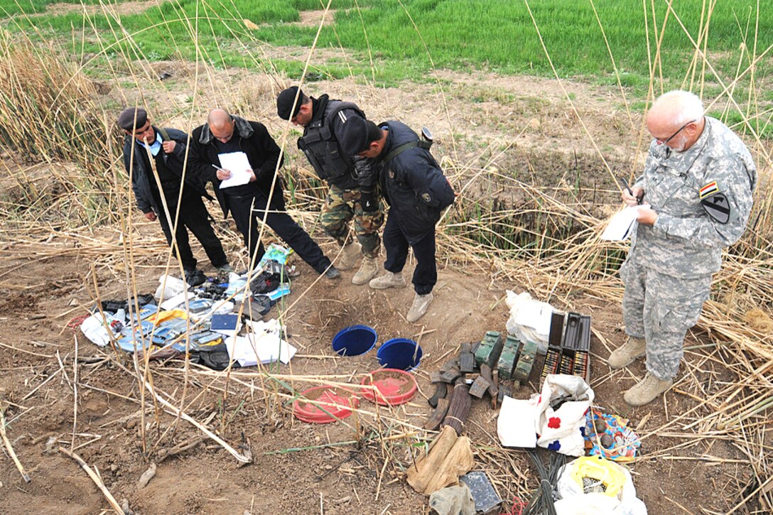 Joe Rouchet, a contracting investigator for U.S. forces, and Iraqi police officers document items found during a weapons cache search of a farmland outside Osharea, Iraq, March 20, 2009.