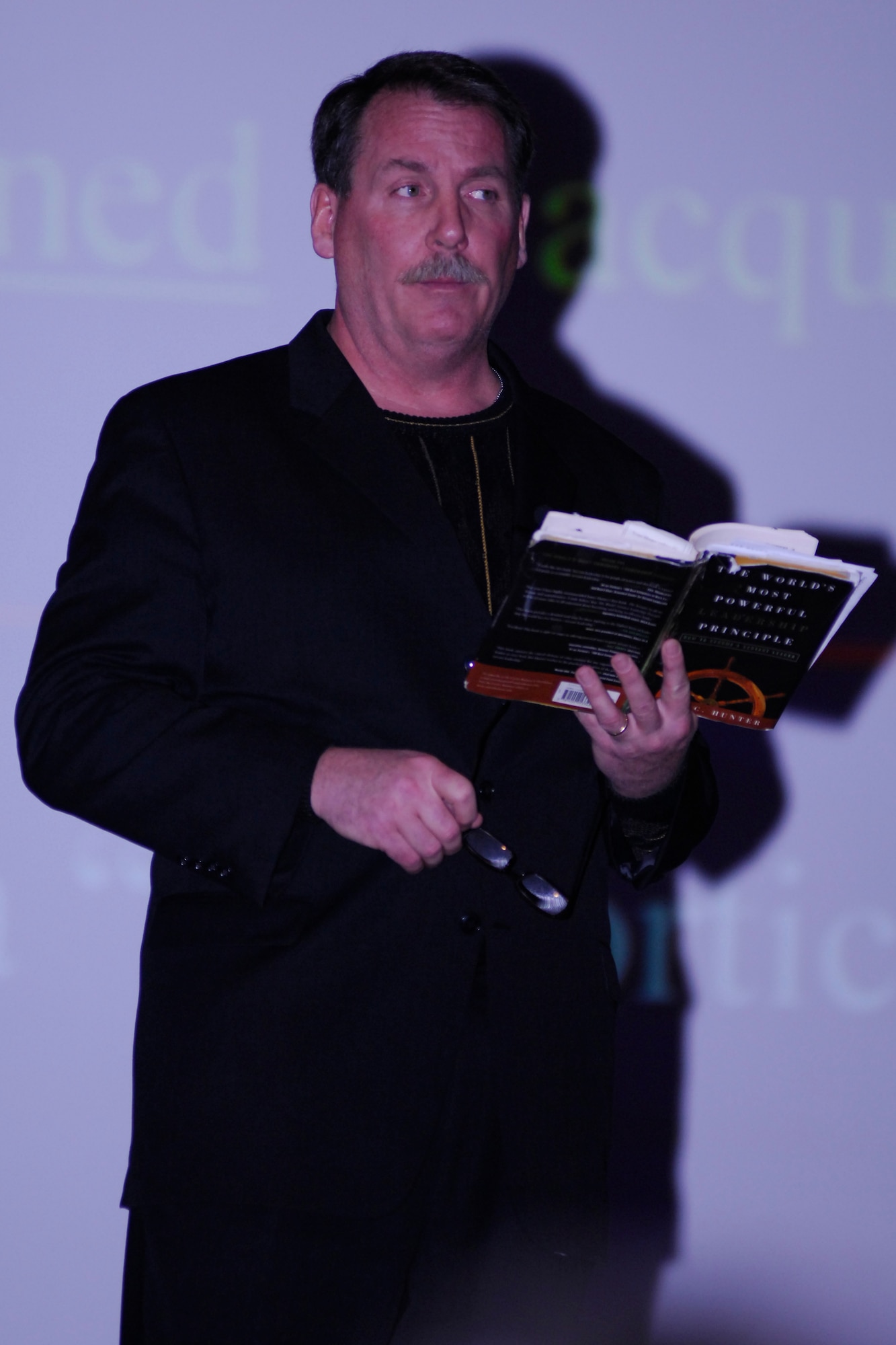 MINOT AIR FORCE BASE, N.D. -- Mr. James Hunter, of J.D. Hunter Associates, LLC, reads from his book titled "The World's Most Powerful Leadership Principle" while he speaks to group of Aimen and civilians at the base theater here March 20. The 5th Mission Support Group brought in Mr. Hunter in an effort to bring in speakers once a quarter to discuss a topic that relates to professional development such as ethics, mentorship, and servant leadership. (U.S. Air Force photo by Staff Sgt. Thomas Dow)