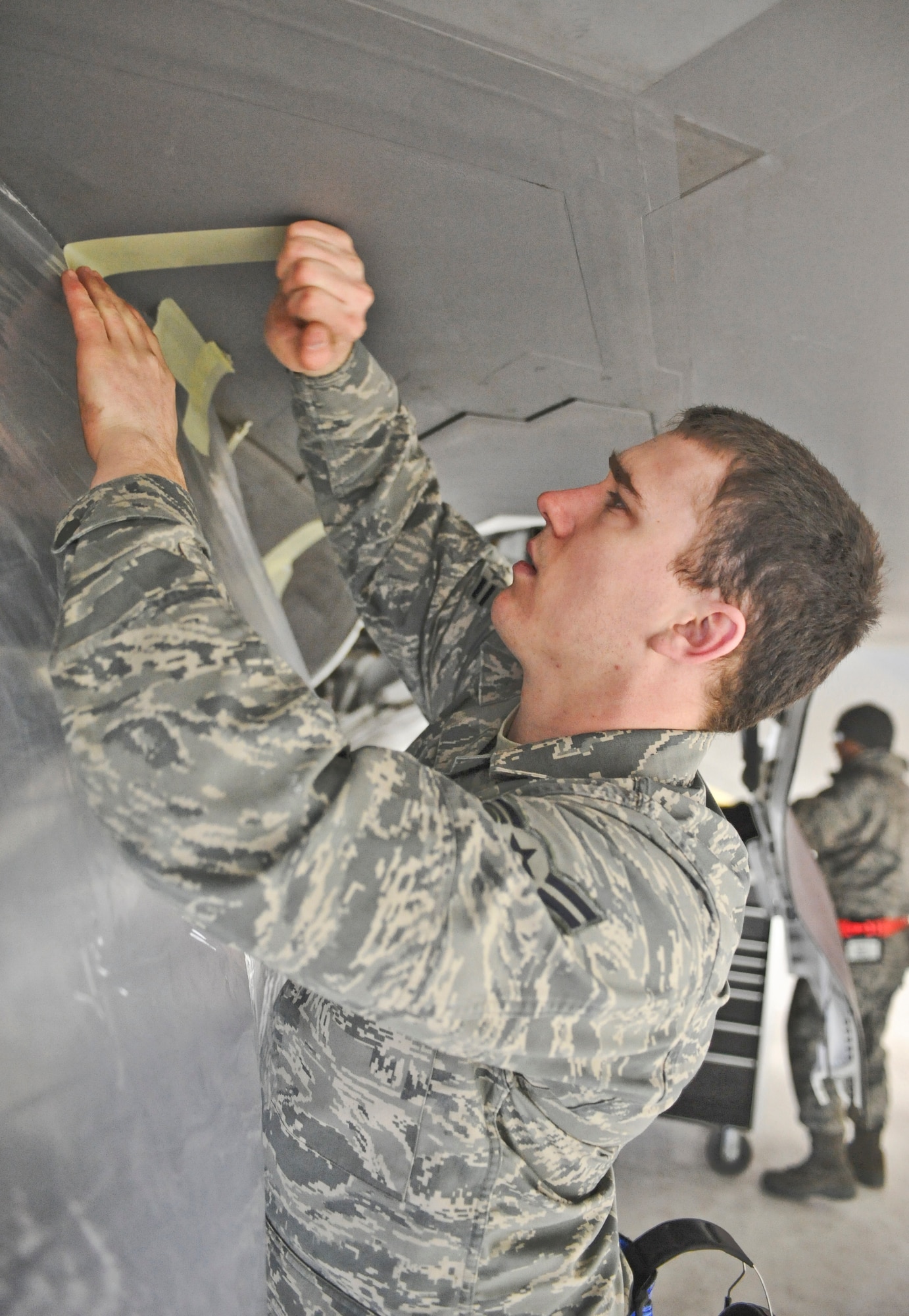 ELMENDORF AIR FORCE BASE, Alaska -- Airman 1st Class Craig Mason, 525th Aircraft Maintenance Unit, tapes plastic an F-22 March 26. Raptors and maintenance equipment from the 525th Fighter Squadron are sheltered inside a hangar due to the ongoing eruptions of Mount Redoubt. (U.S. Air Force photo by Senior Airman Matthew Owens) 