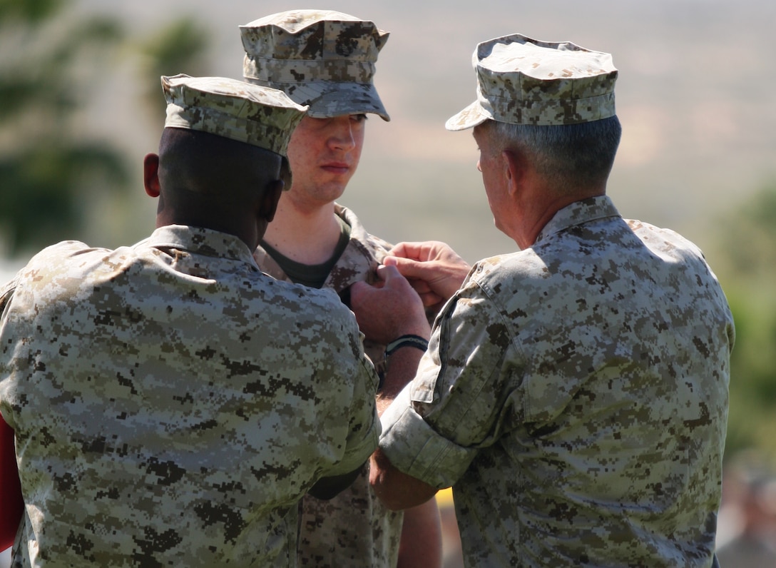 Lance Cpl. Brady Gustafson, a machine gunner with Golf Company, 2nd Battalion, 7th Marine Regiment receives a meritorious promotion to corporal from Maj. Gen. Thomas D. Waldhauser and Sgt. Maj. Randall Carter, the commanding general and sergeant major of 1st Marine Division.