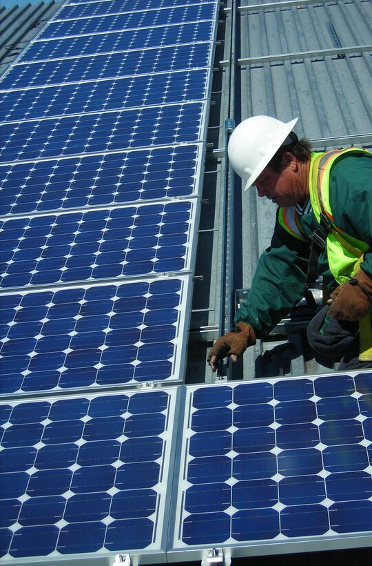 A construction worker installs solar panels on the sun shades in a motor pool at the Combat Center as part of an initiative to triple the amount of renewable energy the base uses.