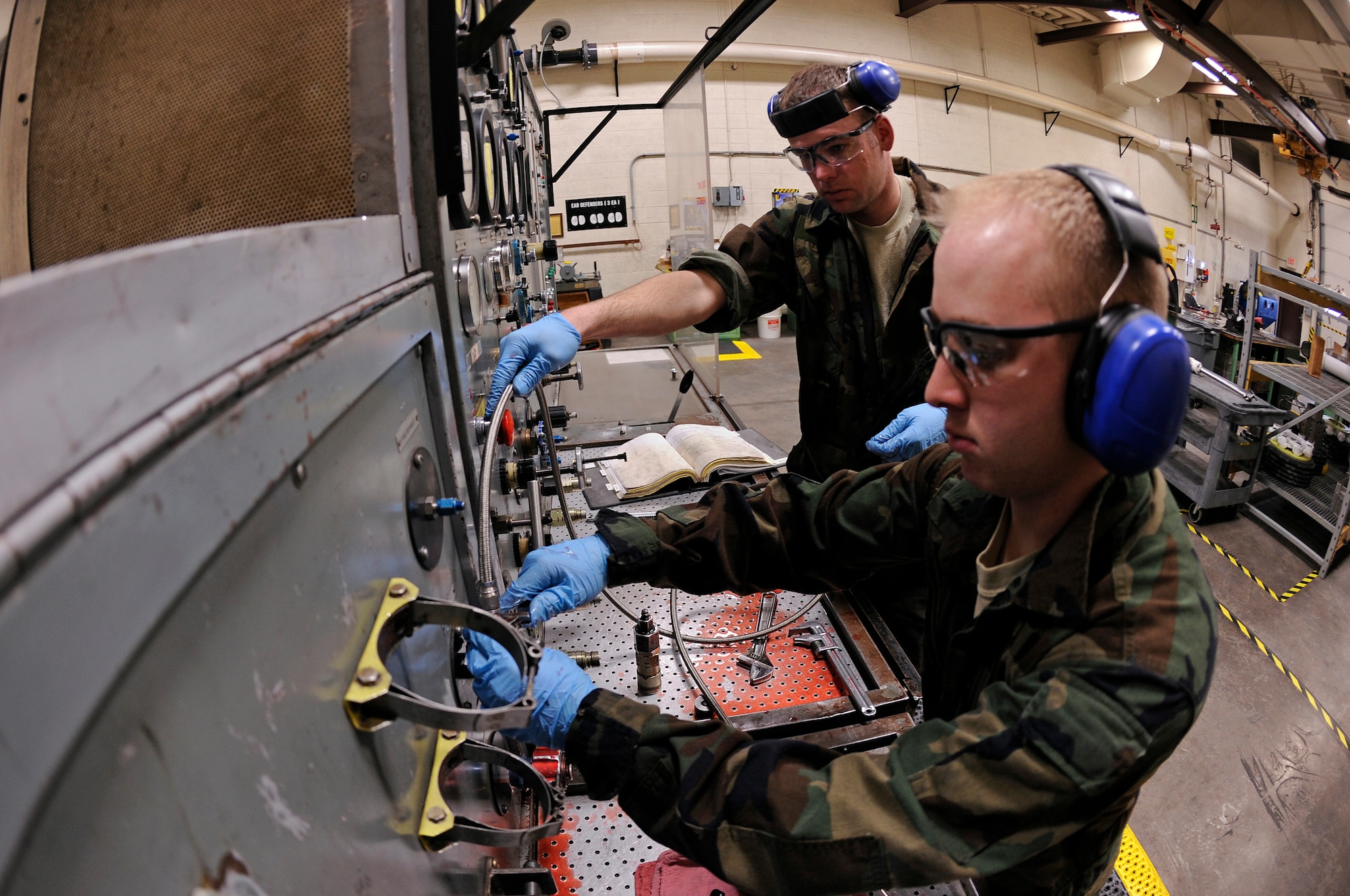 (Back) Staff Sgt. Jon-Michael Rull, 28th Maintenance Squadron hydraulics craftsman, and Airman 1st Class Chad Myers, 28 MXS hydraulics journeyman, prepare to bench test a B-1B Lancer main landing gear emergency accumulator, March 27. The main landing gear emergency accumulator is tested under 6,000 pounds per square inch of pressure to test for piston seizure. (U.S. Air Force photo/Senior Airman Marc I. Lane)