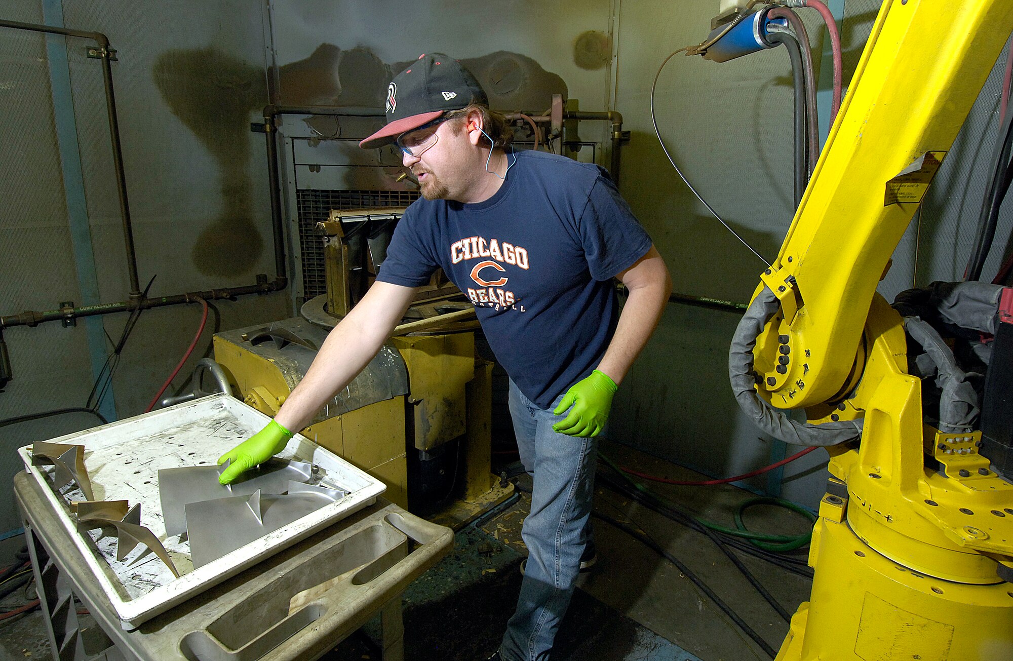 Nicki Kuhn, a metalizing equipment operator, readies F100 first-stage fan blades for plasma spray inside a spray booth.  The yellow robotic arm will apply a  bronze coating build up to each blade. (Air Force photo/Margo Wright)