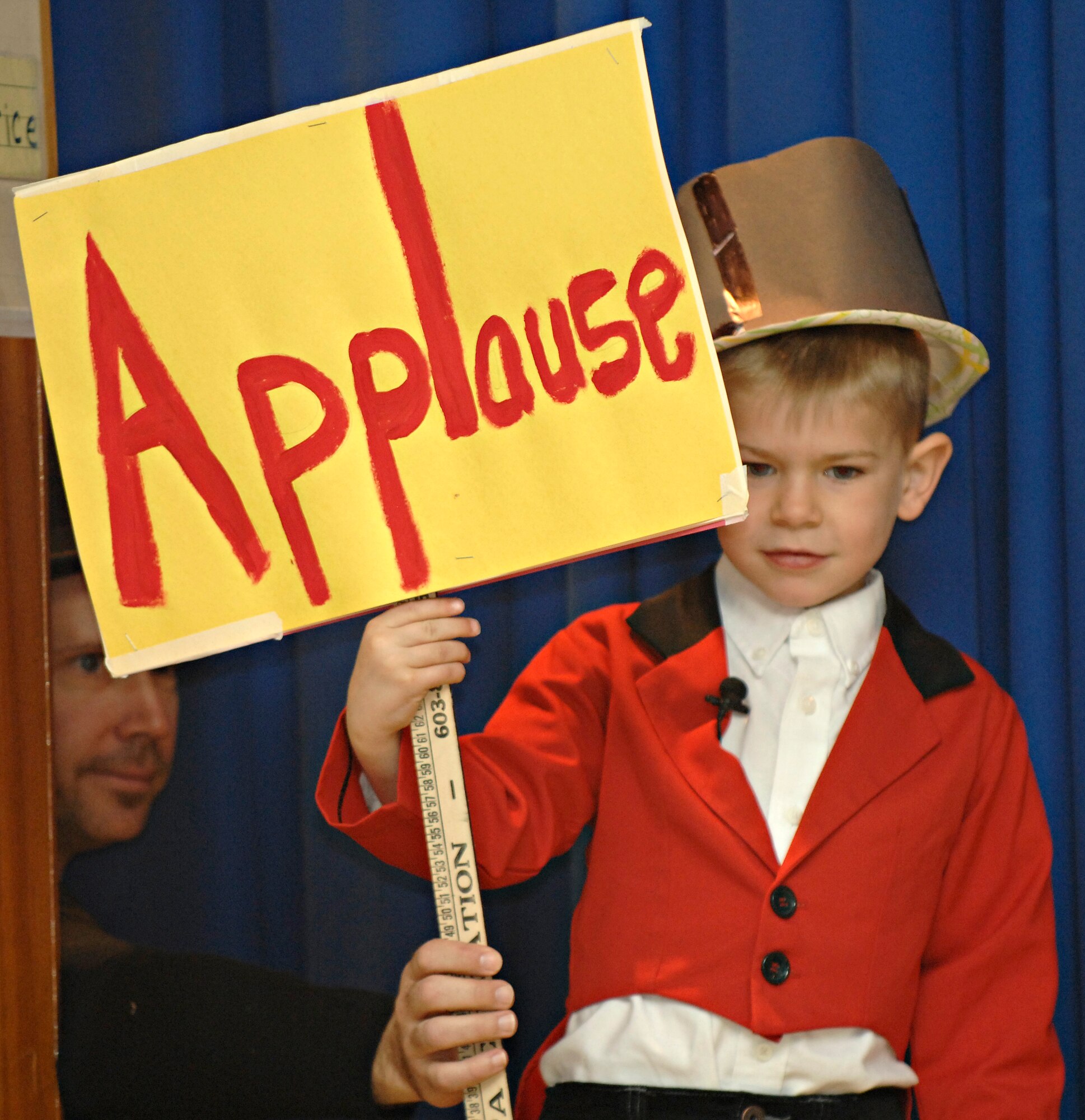 Gavin Riley, son of Staff Sgt. Sarah Donis, 39th Security Forces Squadron, fulfills his duties as ringmaster and holds up an applause sign with a little help from Harry Atkinson, Incirlik Unit School teacher, during the kindergarten circus at the IUS, Friday, March 27, 2009. The children helped design the set, props and costumes, as well as writing the script for the circus they put on for their parents. The whole experience incorporated learning about animals along with math and writing, said Mr. Atkinson. (U.S. Air Force photo/Senior Airman Benjamin Wilson, 39th Air Base Wing Public Affairs)