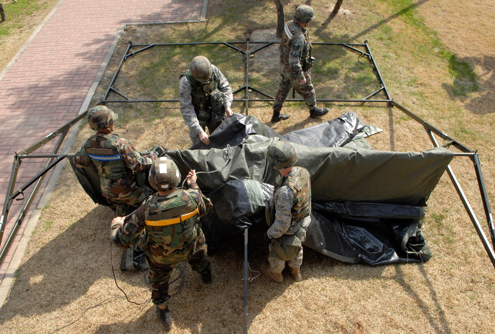 Airmen assemble a tent outside the Osan High School March 29, in preparation for a Noncombatant Evacuation Exercise held at Osan AB, Republic of Korea. A NEO exercise tests a bases capability to evacuate nonessential personnel from a location in a host foreign nation to a safe haven. The NEO was part of a pre-scheduled exercise to preparae for the Operational Readiness Inspection the 51st Fighter Wing will undergo in April. (U.S. Air Force Photo/Staff Sgt. Brian Ferguson) 