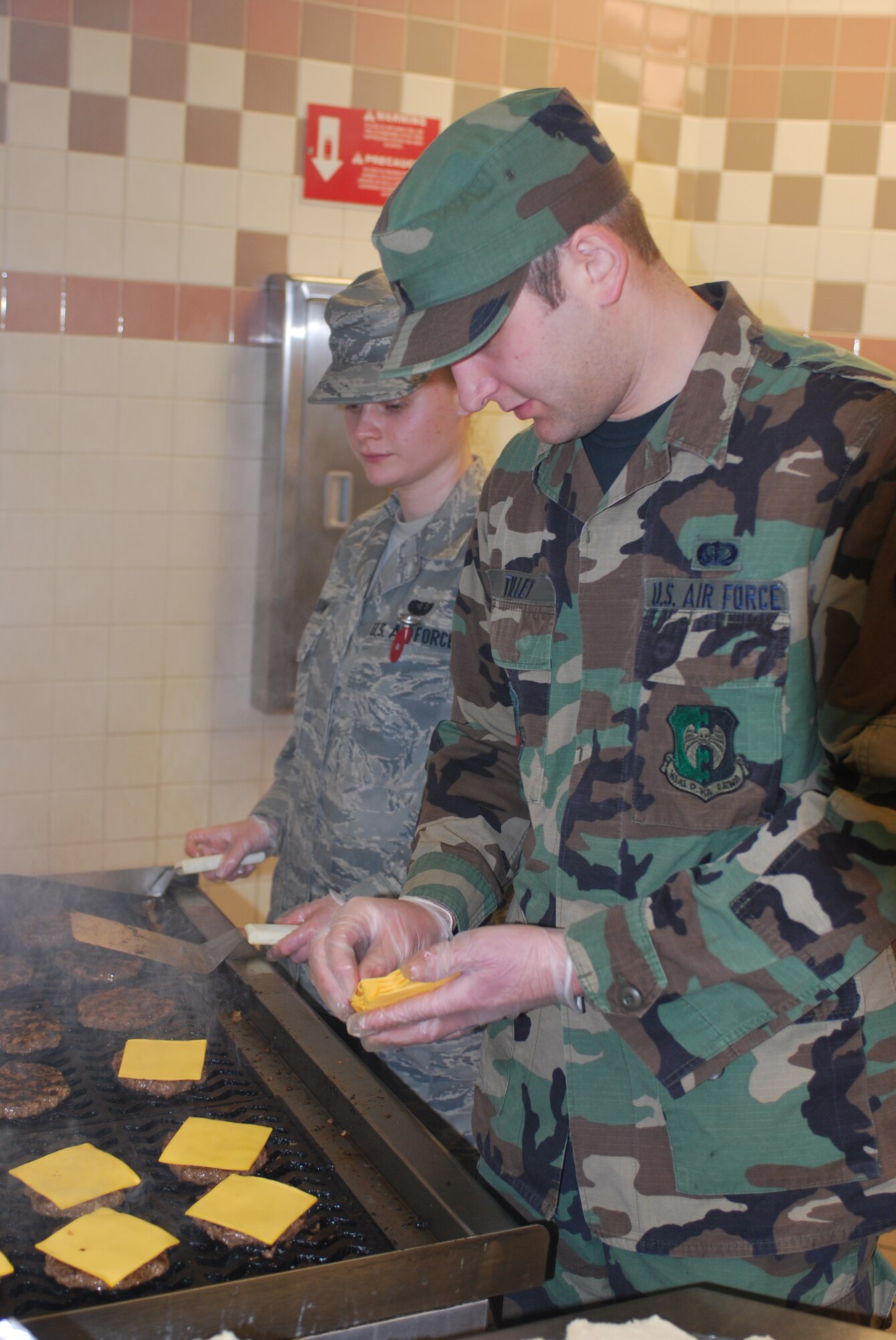 GRAND FORKS AIR FORCE BASE, N.D. -- Airman 1st Class Darren Tilley (right), a chef from the 5th Force Support Squadron at Minot Air Force Base, helps Airman 1st Class Cassandra Allison, a chef from the 319th Force Support Squadron here, make some cheeseburgers at the Airey Dining Facility here March 31st. Currently, 23 Airmen from Minot’s 5th Mission Support Group are helping their fellow Airmen manage the high level of activity on the base due to the influx of servicemembers supporting the flood relief efforts along the Red River. (U.S. Air Force photo by Airman 1st Class Joshua Rosales)