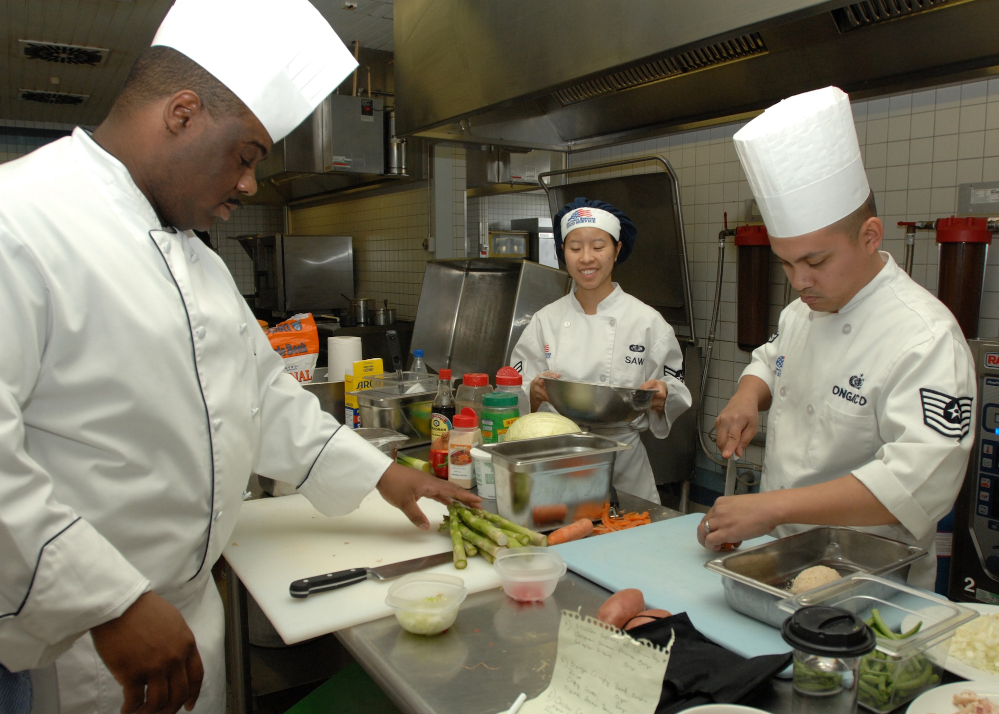 SPANGDAHLEM AIR BASE, Germany -- Team Buechel members Master Sgt. Christopher Roger and Tech. Sgt. Rommel Ongaco, both from the 702 Munitions Maintenance Squadron, prepare vegetables. Airman 1st Class Kaythi Saw, 52nd Force Support Squadron, stands by with a bowl during the Iron Chef competition at the Mosel Dining Facility March 30, 2009. Team Buechel won the title of Iron Chef after creating a winning combination of chicken cordon bleu, orange rice with crispy beef and mushroom stuffed chicken. (U.S. Air Force photo by Senior Airman Jenifer H. Calhoun)