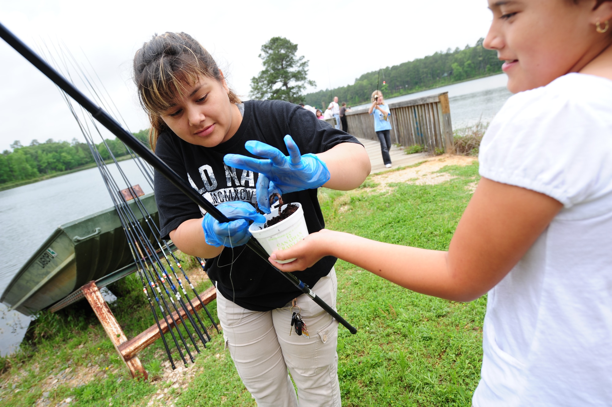 Amelia Lirha assists her daughter, Desiree Romo, 10, by putting a worm on her hook during the Kids Fish event held at Harmon Lake. This was a large role for many of the parents whose children were squeamish of touching the worms. (U.S. Air Force photo by Senior Airman Joanna M. Kresge)