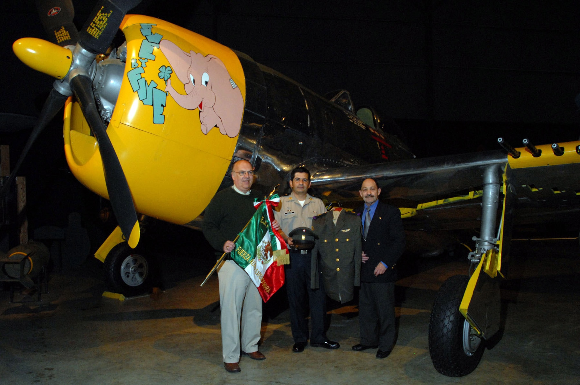 Terry Aitken (left to right), Mexican air force Lt. Col. Daniel Mojica and retired U.S. Air Force Col. Rafael Ramos stand in front of the museum's P-47, the same type of aircraft Mexican Fighter Squadron 201 flew during World War II, while holding some of the items that were donated during a ceremony April 29 at the National Museum of the U.S. Air Force in Dayton, Ohio. Mr. Aitken is the senior curator for the museum. (U.S. Air Force photo) 
