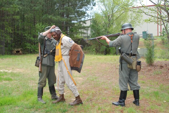Master Sgt. Michael Varnado, 700th Airlift Squadron Life Support  NCO, reenacts a scene of a Tuskegee Airman fighter pilot being taken prisoner by German Soldiers after being shot down in Europe during World War II.
The reenactment took place at the Annual World War II Heritage Days event at Peachtree City Airport April 19.  The Commemorative Air Force Dixie Wing, a local patriotic organization hosted its sixth annual event on April 18-19 to pay tribute to the veterans of WWII and all of America’s veterans.
Clayton David (left) and Austin Arrington (right) reenact the actions of WWII German Army grenadier privates on patrol.  Arrington, whose reenactment name is “Erick Reicher” keeps a rifle on the Tuskegee Airman while David, whose reenactment name is “Eugen Foerster,” has the pilot to remove his flight jacket during the search for weapons and information.  (U.S. Air Force photo/Master Sgt Stan Coleman)
